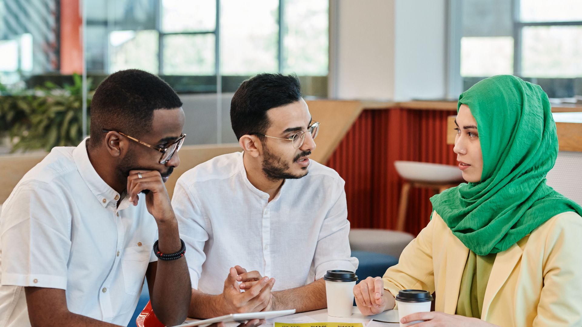 Three diverse colleagues in a modern office having a focused conversation around a table.