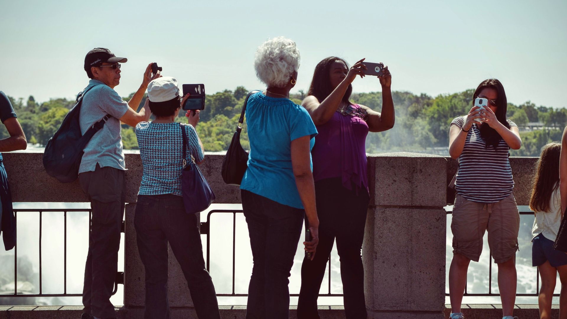 Group of diverse tourists using smartphones to capture scenic outdoor views on a sunny day.