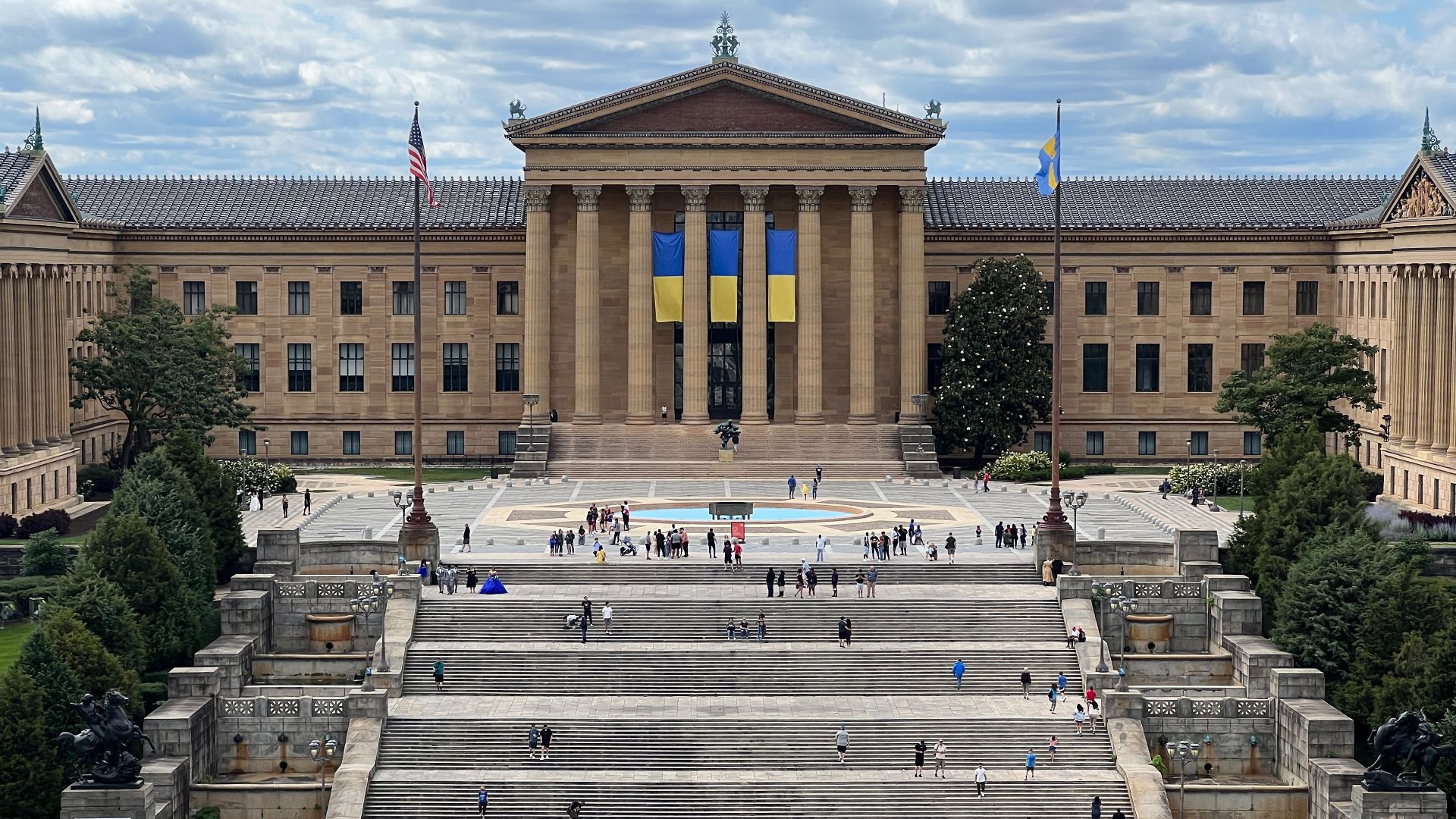 Main building of the Philadelphia Museum of Art, with banners of the Ukrainian flag.  Taken on June 18th, 2022 from the top of the carousel in The Oval XP, an eight-acre warm-weather urban oasis on the Benjamin Franklin Parkway.