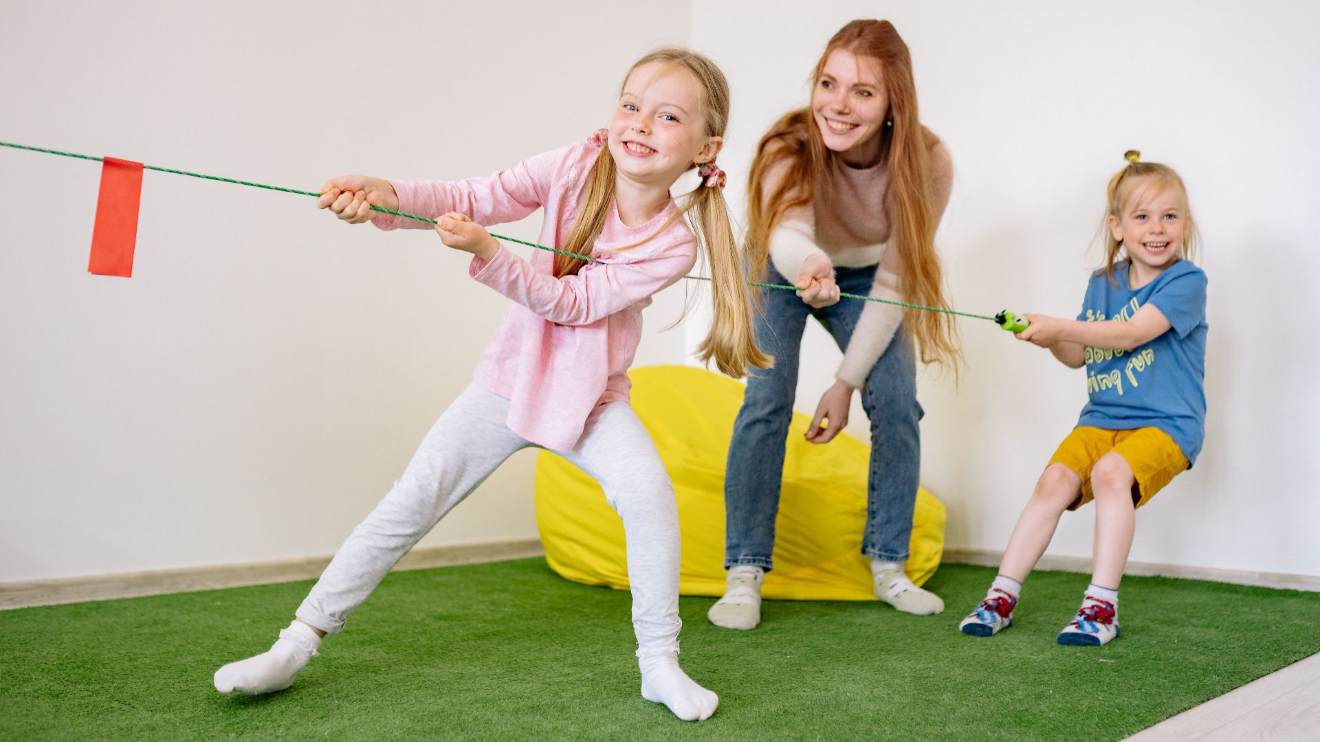 Kids and teacher enjoying a fun tug-of-war game in an indoor playroom setting.