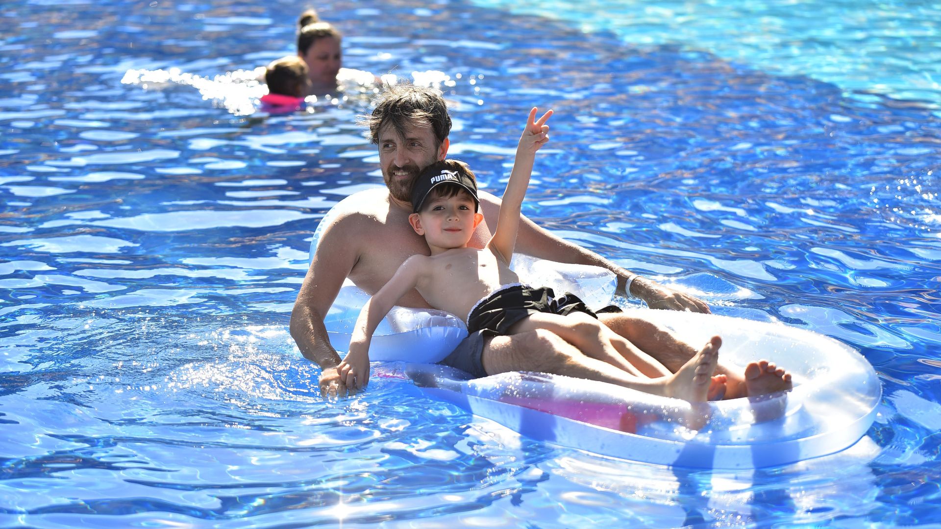 Father and son enjoying summer on an inflatable mattress in a sunny pool.