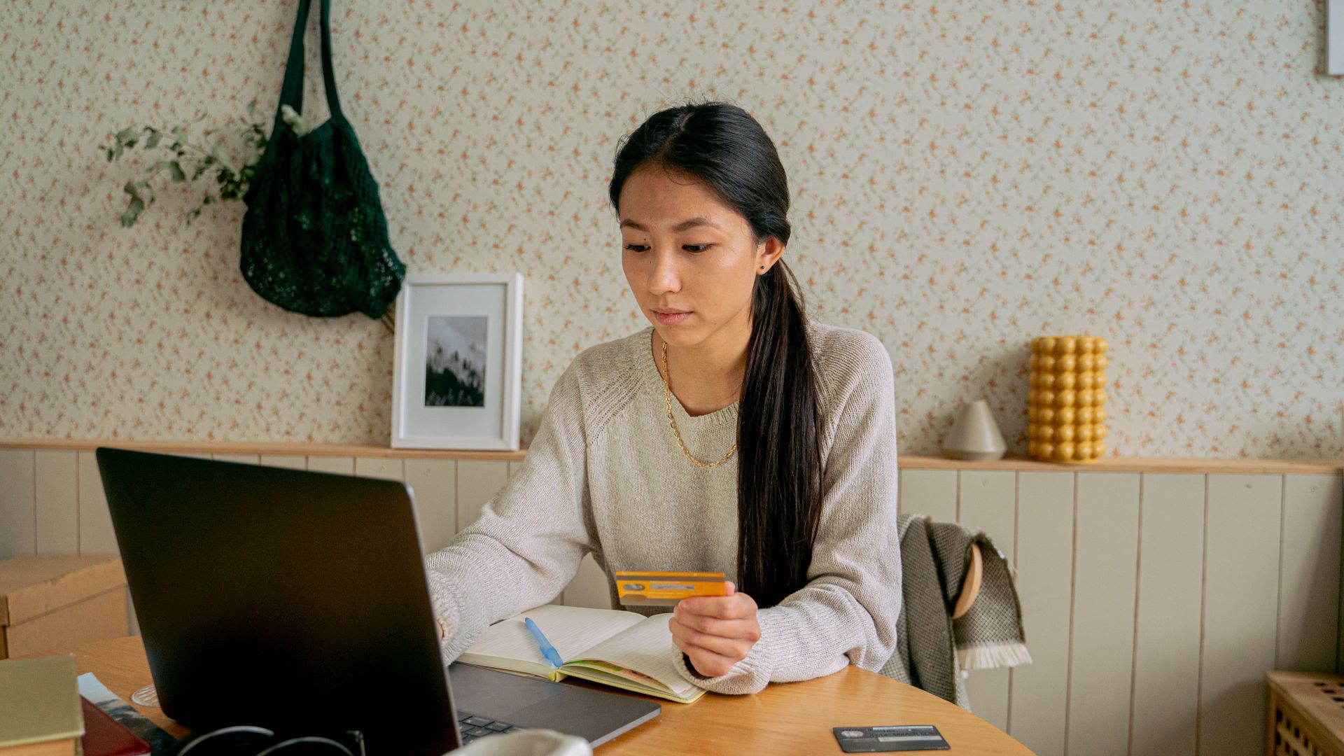 A woman using a laptop and credit card for online shopping at a cozy indoor setting.