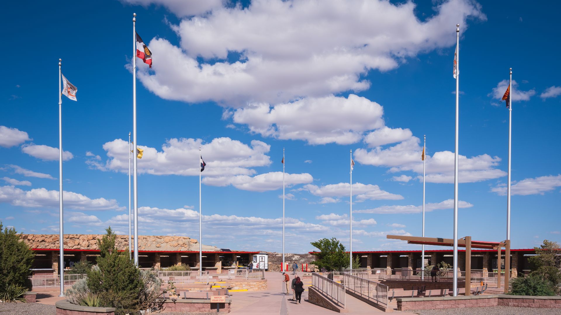 View of the Four Corners Monument plaza from the southern walkway, showing the open galleries housing the Navajo and Ute craft stalls, the stone terraces and the flagpoles.