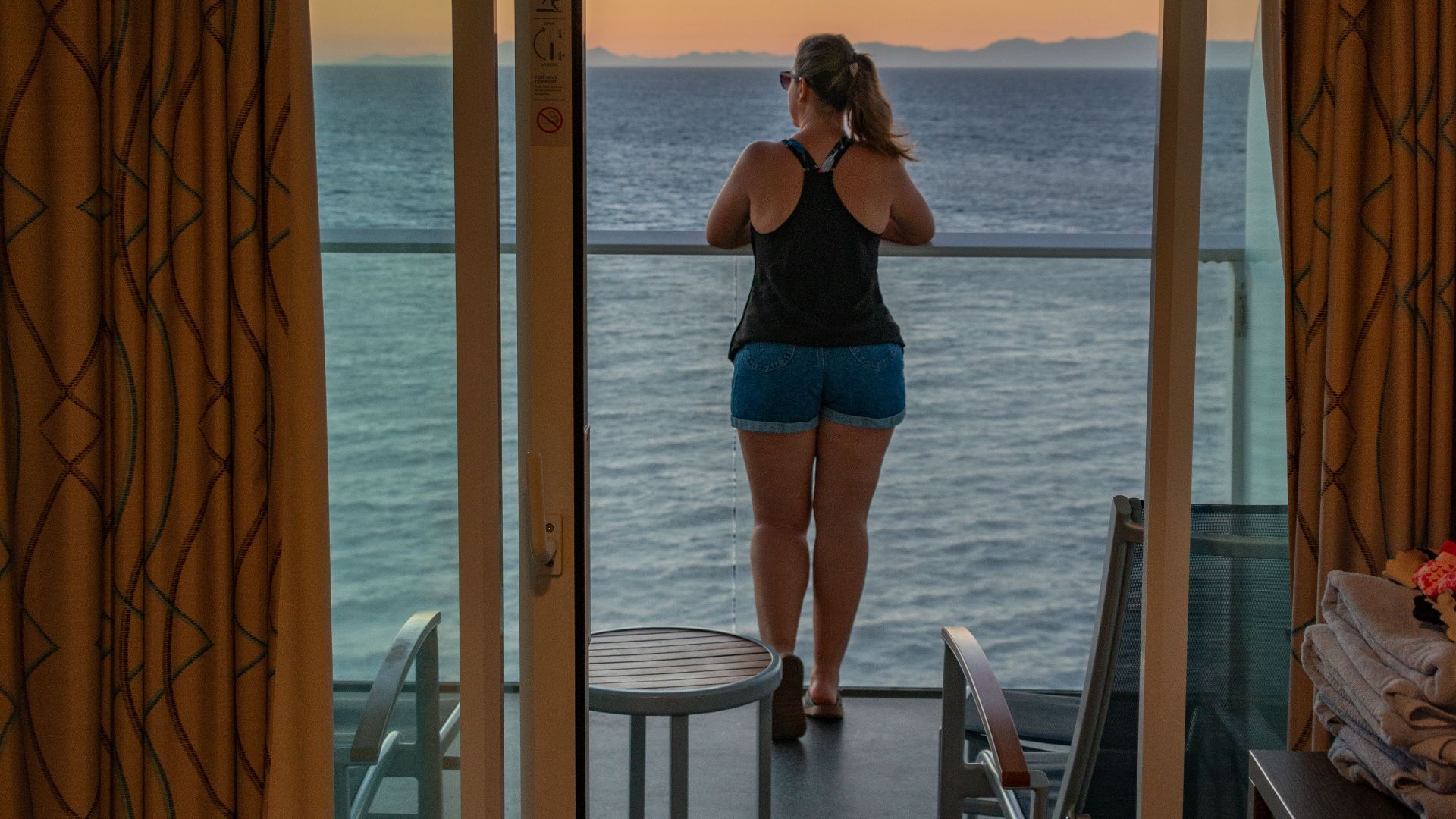 A woman enjoys a serene sea view from a balcony at sunset, capturing a moment of relaxation.
