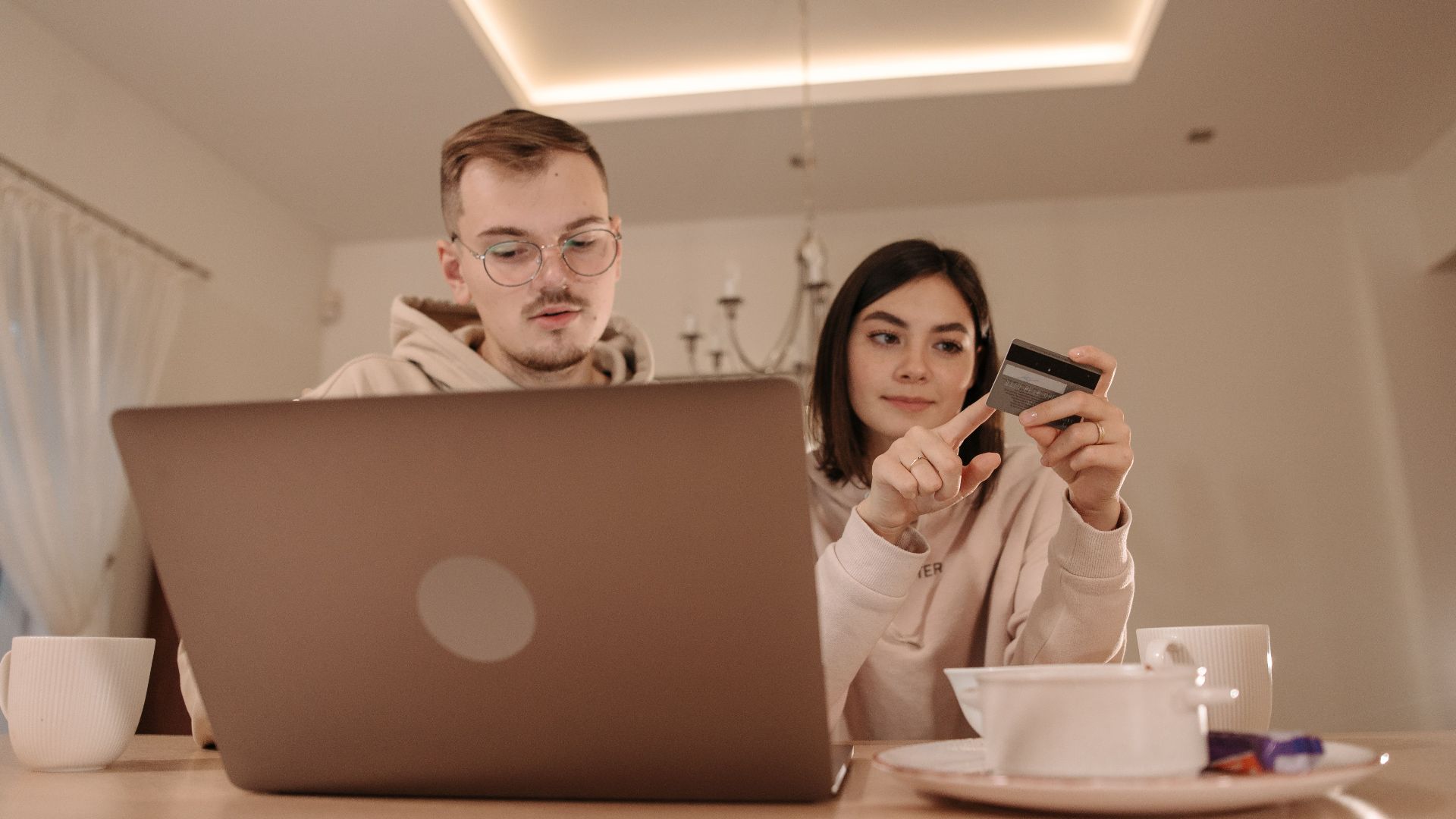 A young couple using a laptop and credit card for online shopping in a cozy indoor setting.