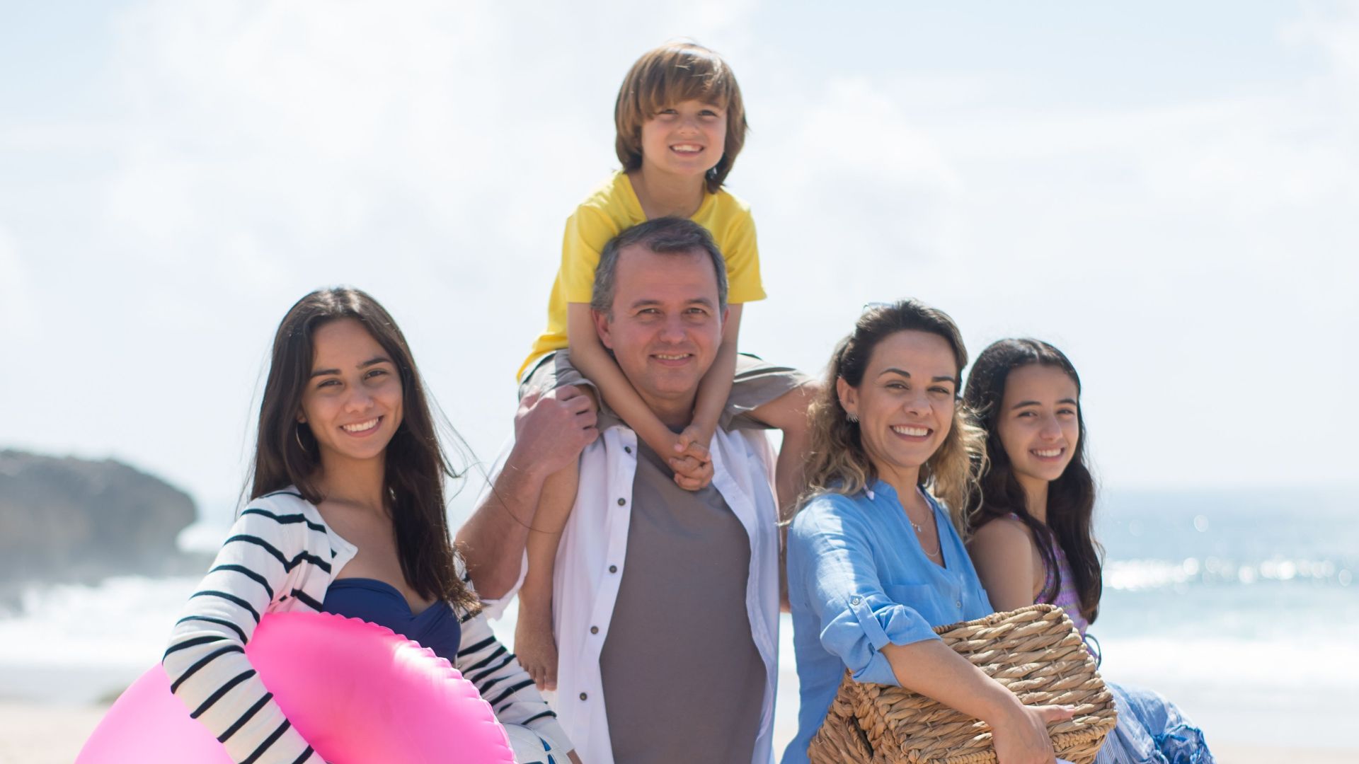 A family of five posing happily on a sunny beach in Portugal, capturing summer memories.