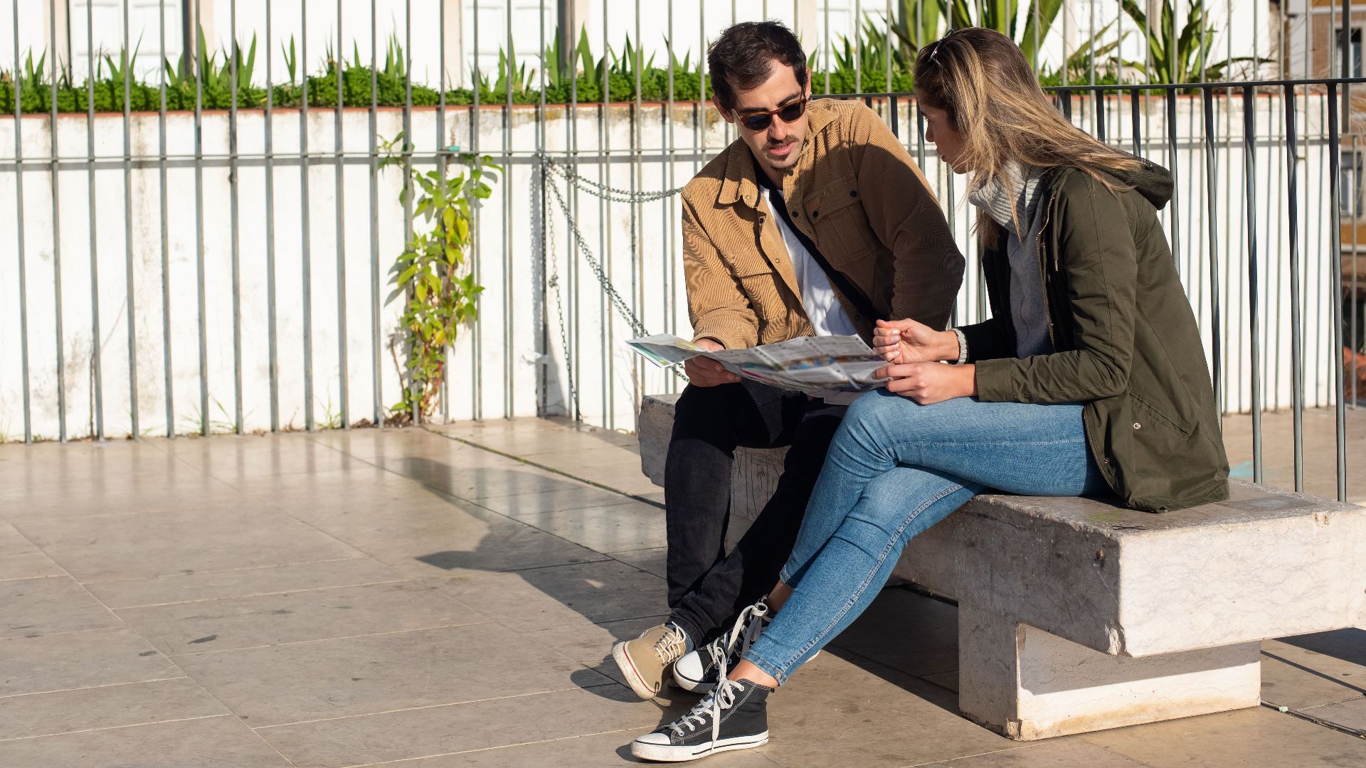 A couple of tourists sitting on a bench, studying a map on a sunny day.