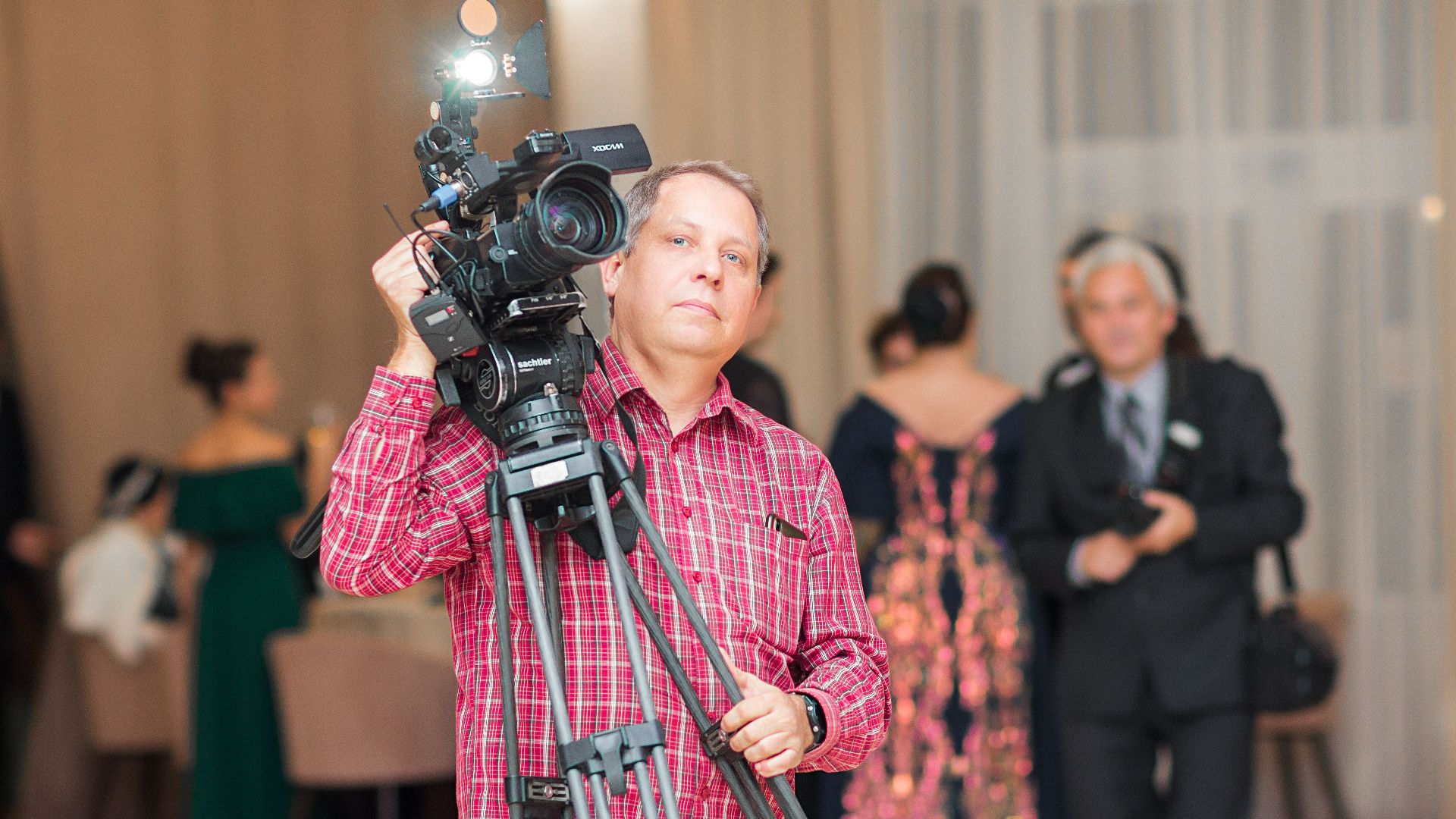 Cameraman capturing moments at a formal indoor event with elegant attire and professional equipment.