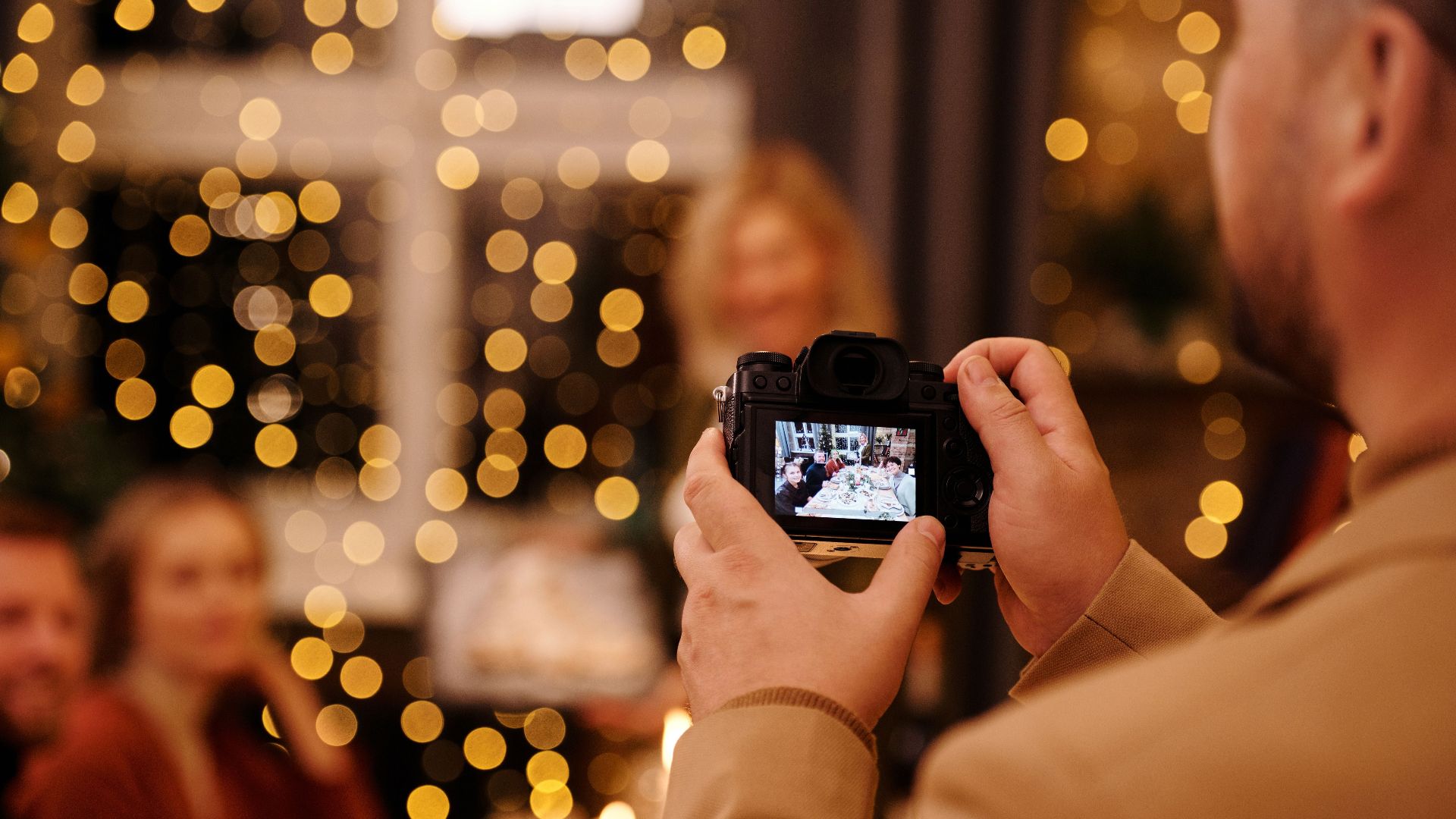 Man capturing a family dinner gathering with a camera surrounded by warm festive lights.