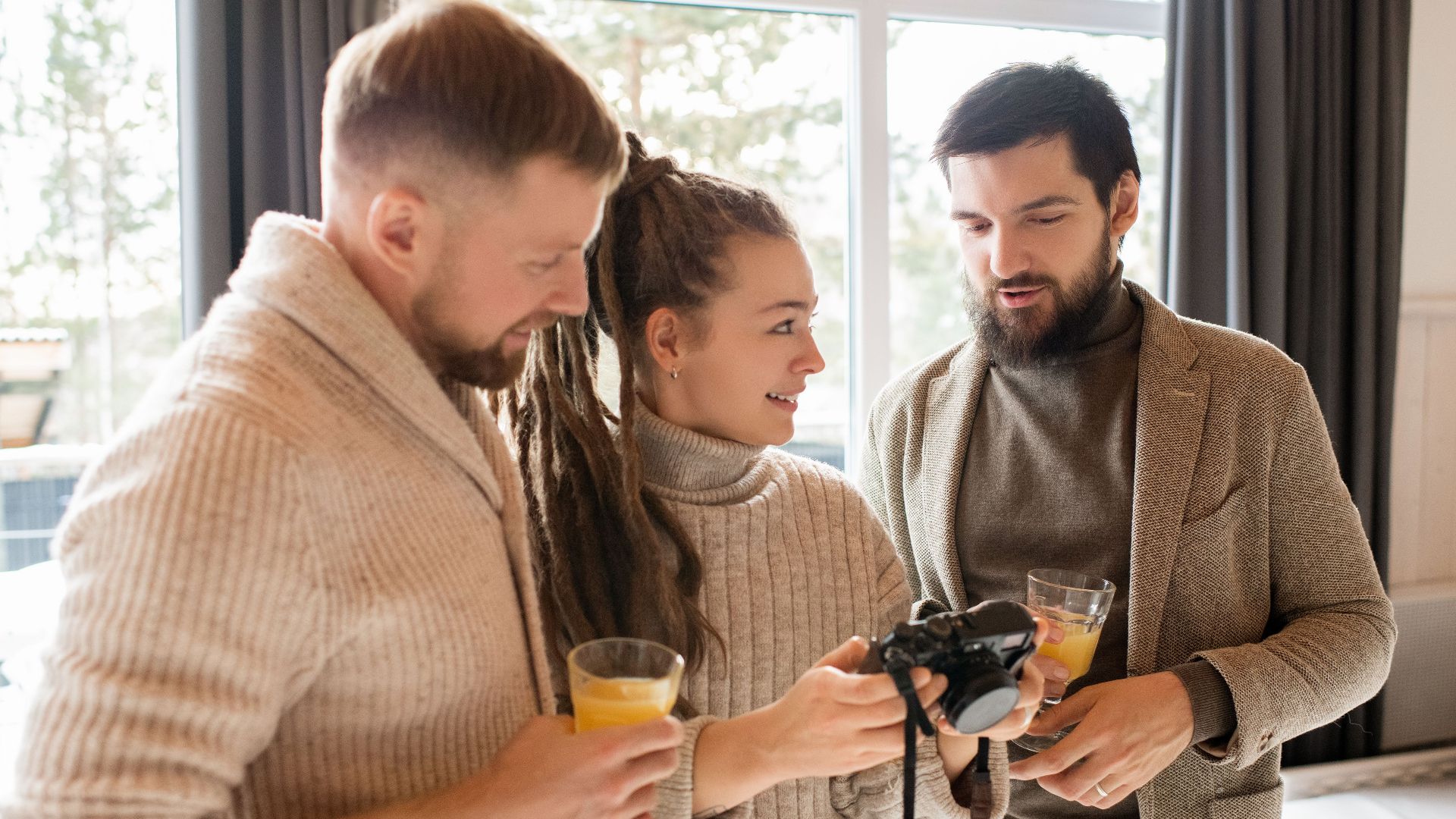 Three adults enjoy a casual indoor gathering while discussing camera settings over drinks.