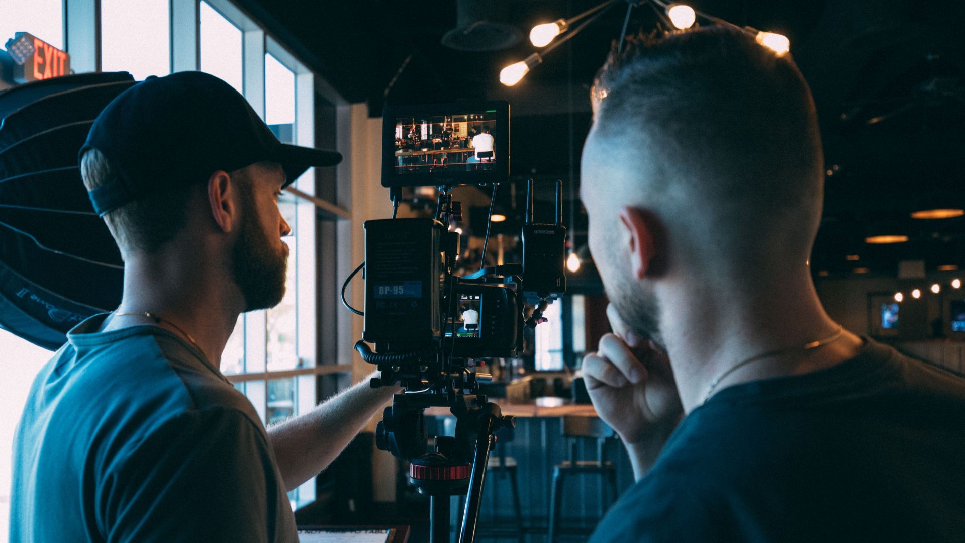 Two filmmakers adjusting camera equipment indoors for a shoot, focusing on cinematography.