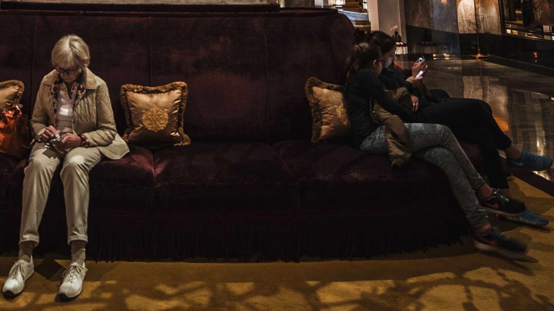 Unrecognizable people sitting on comfortable sofa in spacious hall of luxury hotel with crystal chandeliers and marble statue