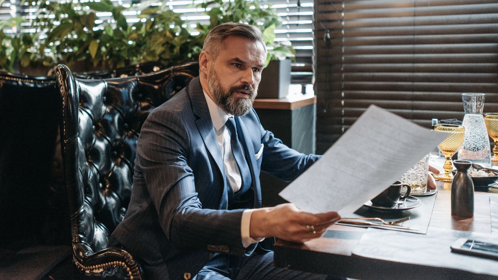 Elderly businessman in a suit analyzing paperwork in a modern office with plants.