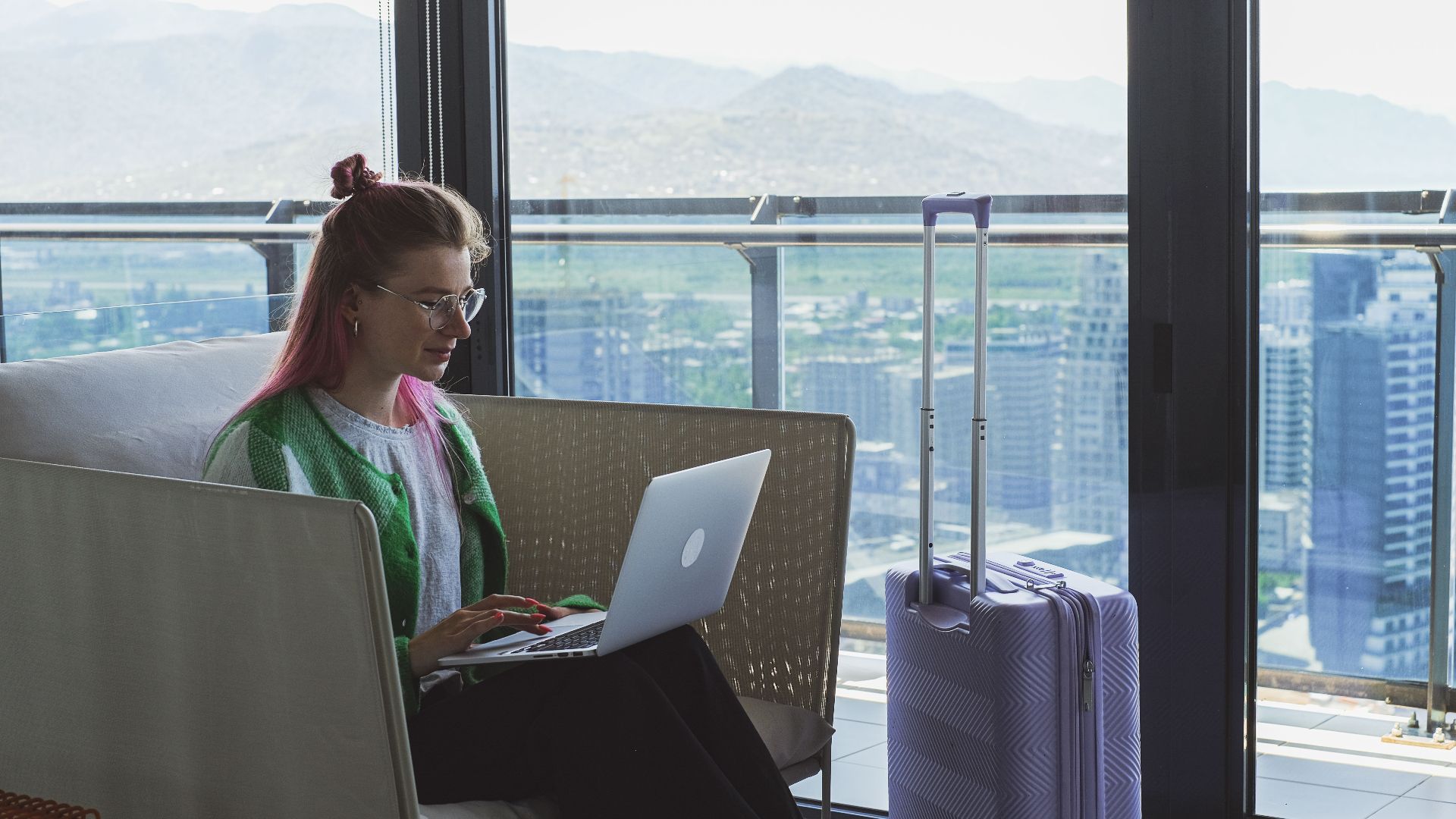 Woman working on a laptop in a hotel lounge with a stunning city view.