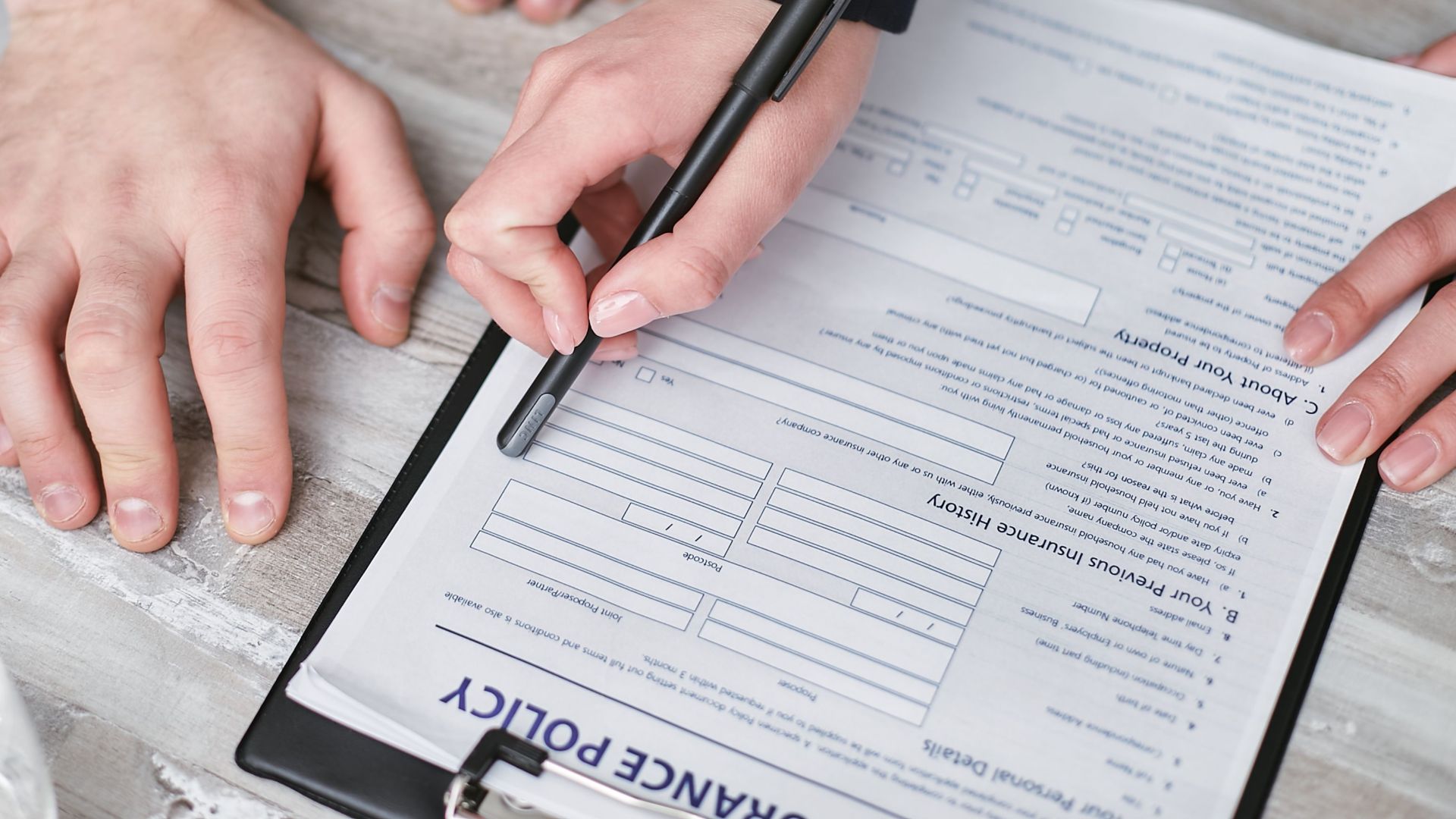 Close-up image of two people signing an insurance policy document on a wooden desk.