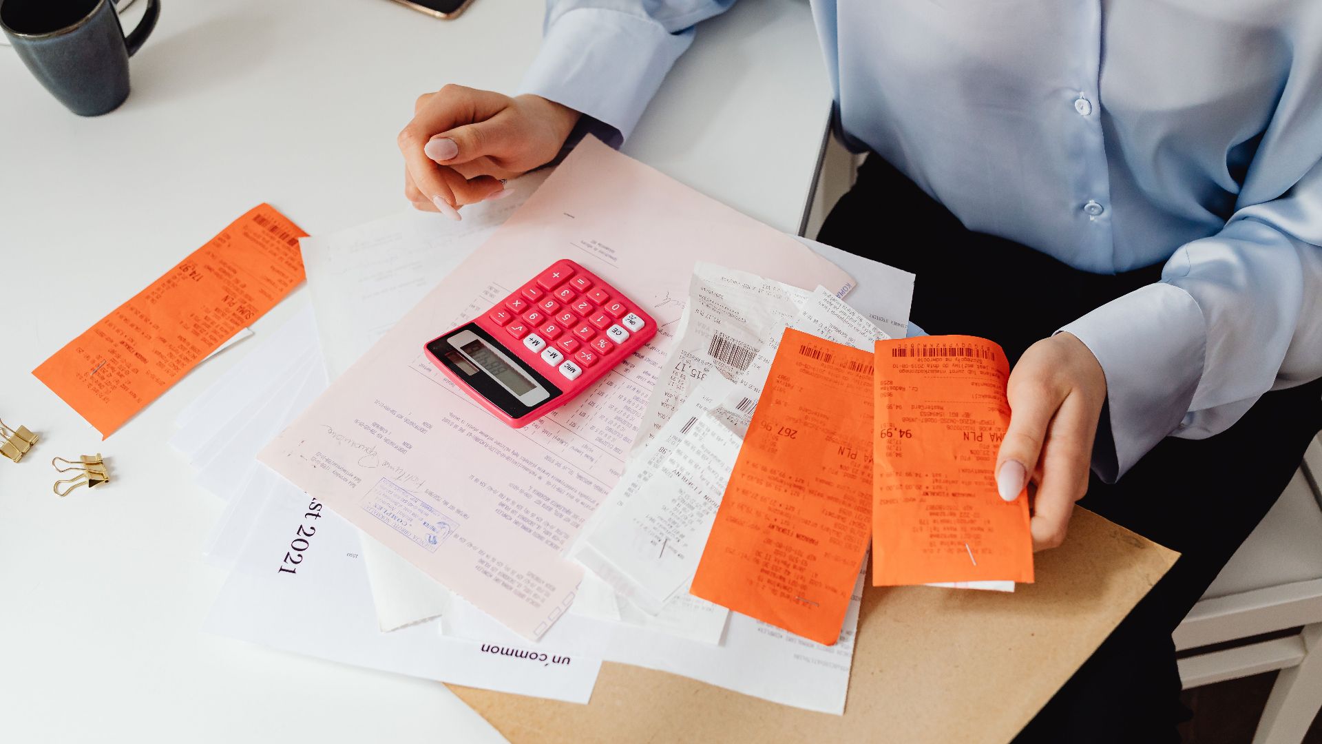A woman reviews receipts and calculates expenses at a desk with a pink calculator.