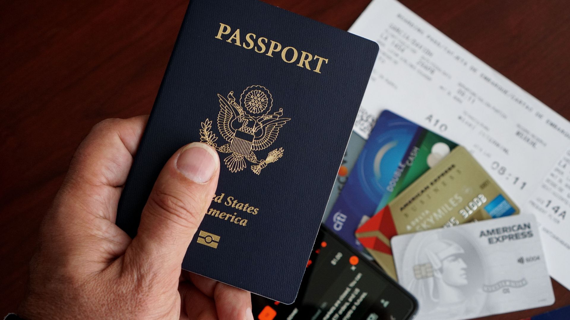 A close-up of a US passport with credit cards, tickets, and a mobile phone on a table.