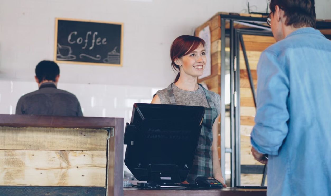A smiling barista assists a customer at a coffee shop counter, creating a warm atmosphere.