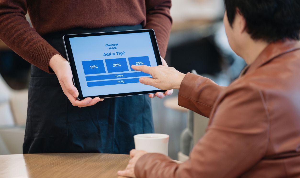 Employee holding tablet for tip payment in cafe and customer touching it to pay tip