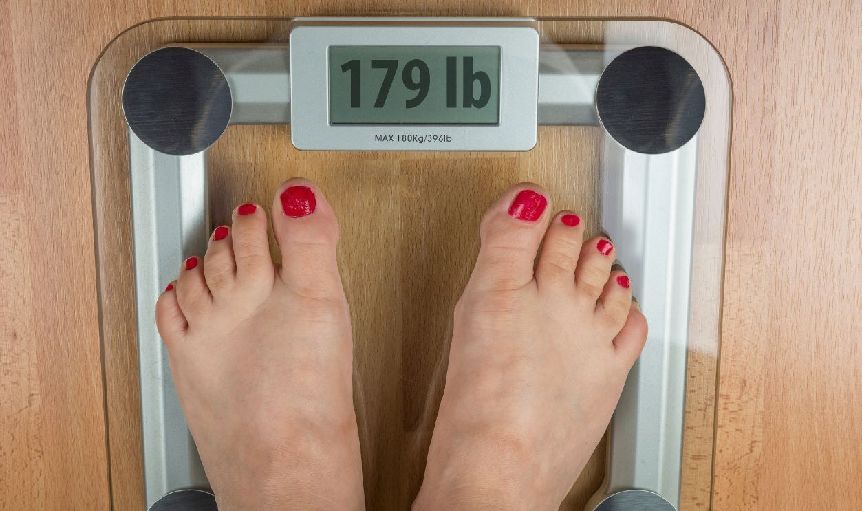 A woman stands with two feet on a scale. Overweight concept