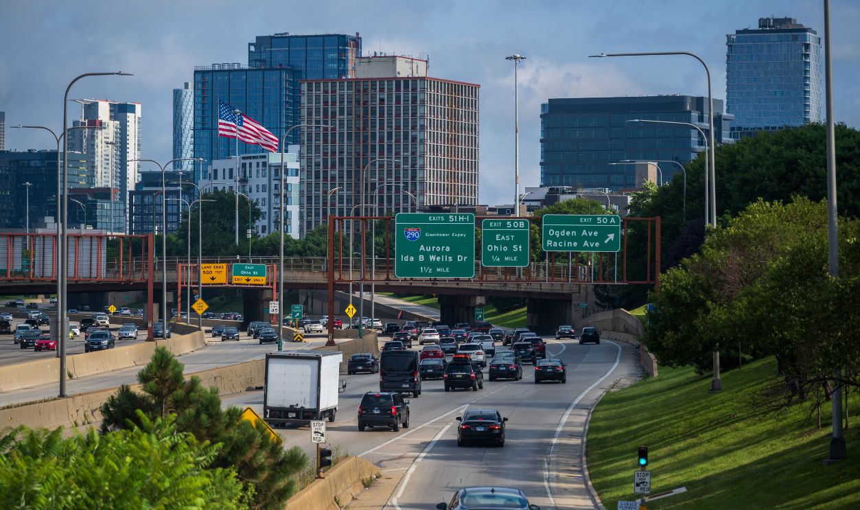 Traffic flows on a Chicago highway with a backdrop of modern skyscrapers and clear signage