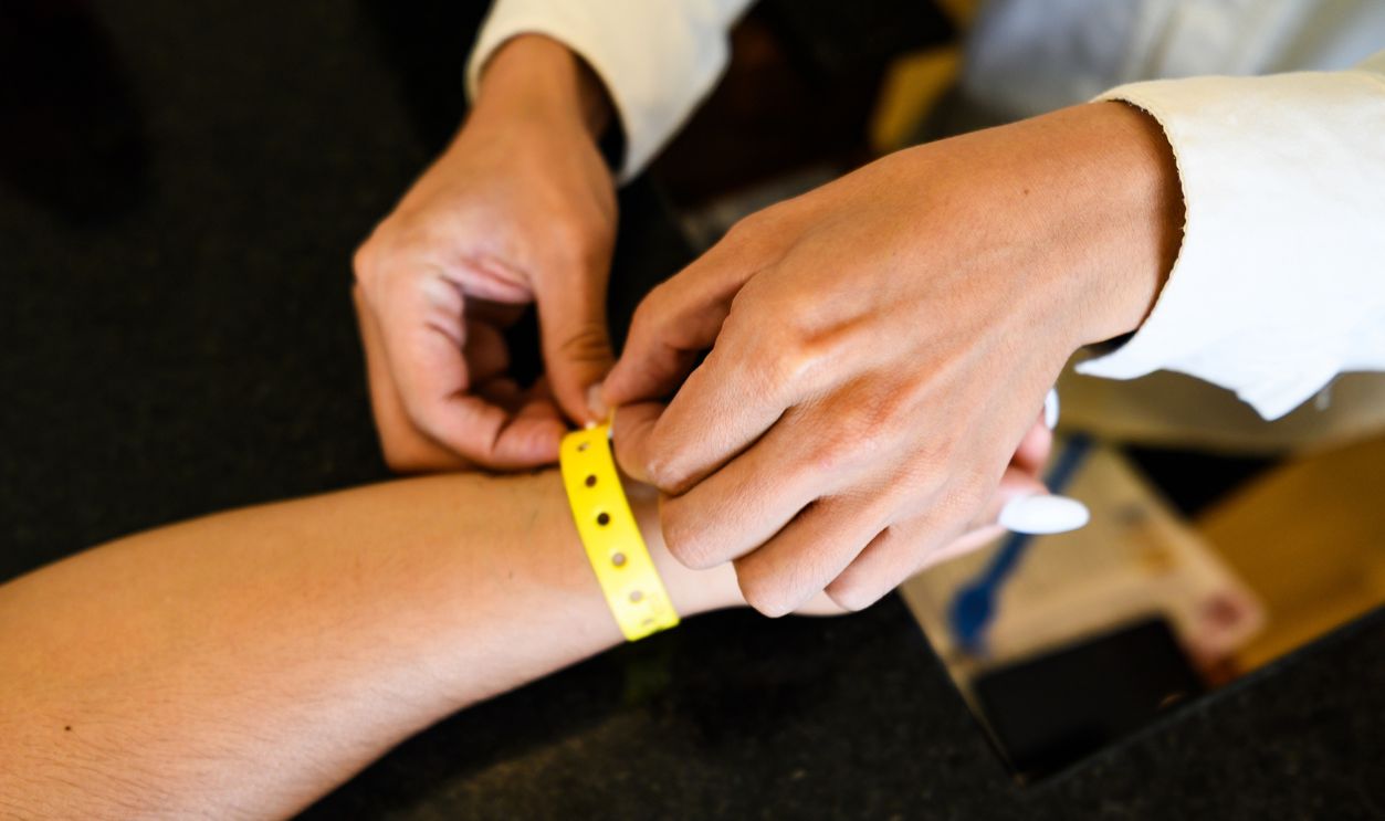 A close-up shot of a hotel staff member or receptionist securing a yellow identification wristband on a tourist's arm.