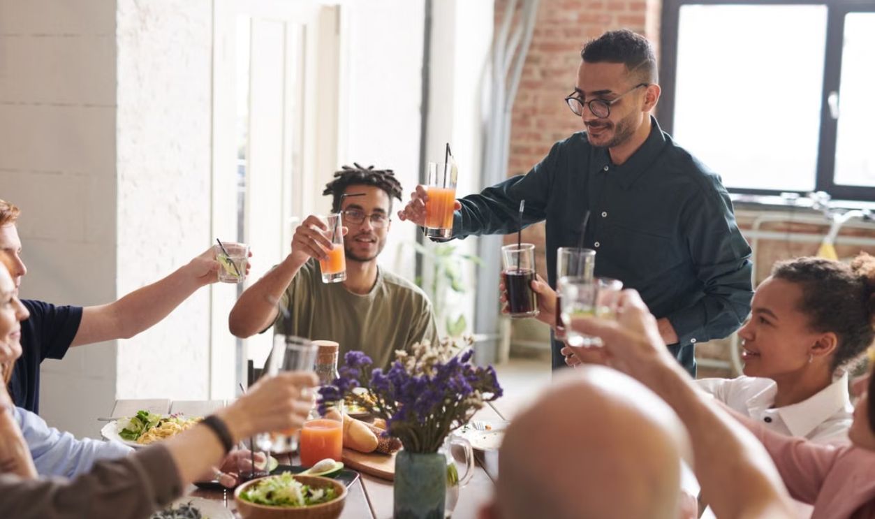 Group of friends toasting drinks during a lively indoor meal, enjoying togetherness and celebration.