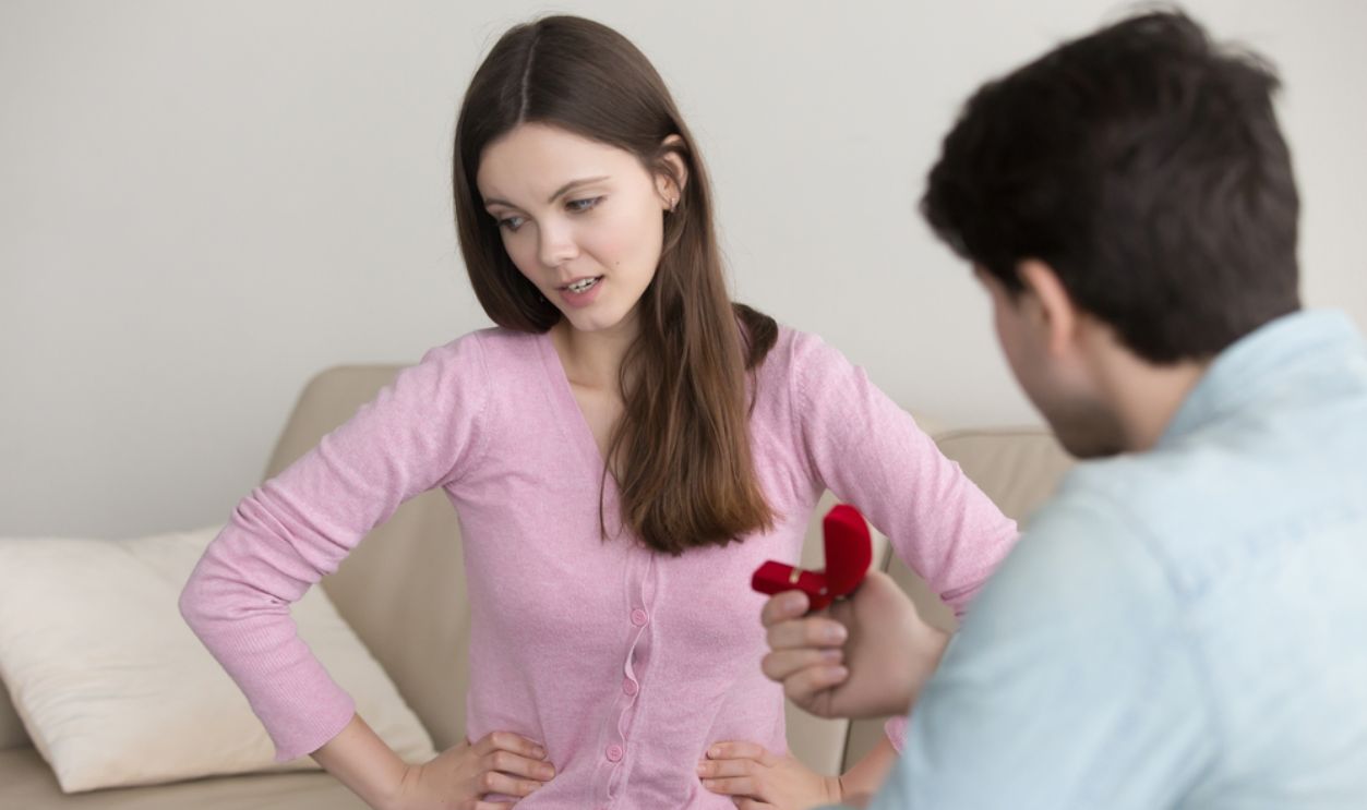 Young man proposing to girlfriend, asking to marry, engagement ring box. Lady hesitating, having doubt, reluctant, thinking of refusal. Unpleasant surprise, bad birthday gift, disappointment in love