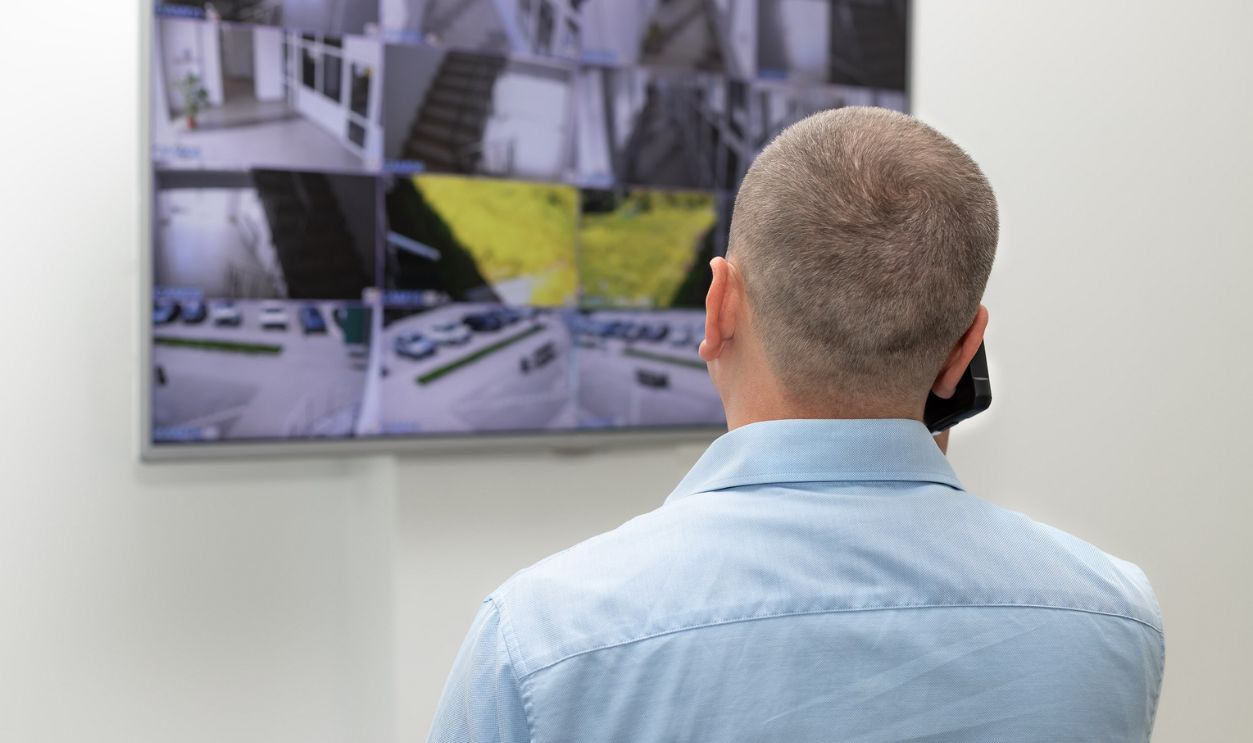 Man is looking at CCTV monitor and talking on the phone.