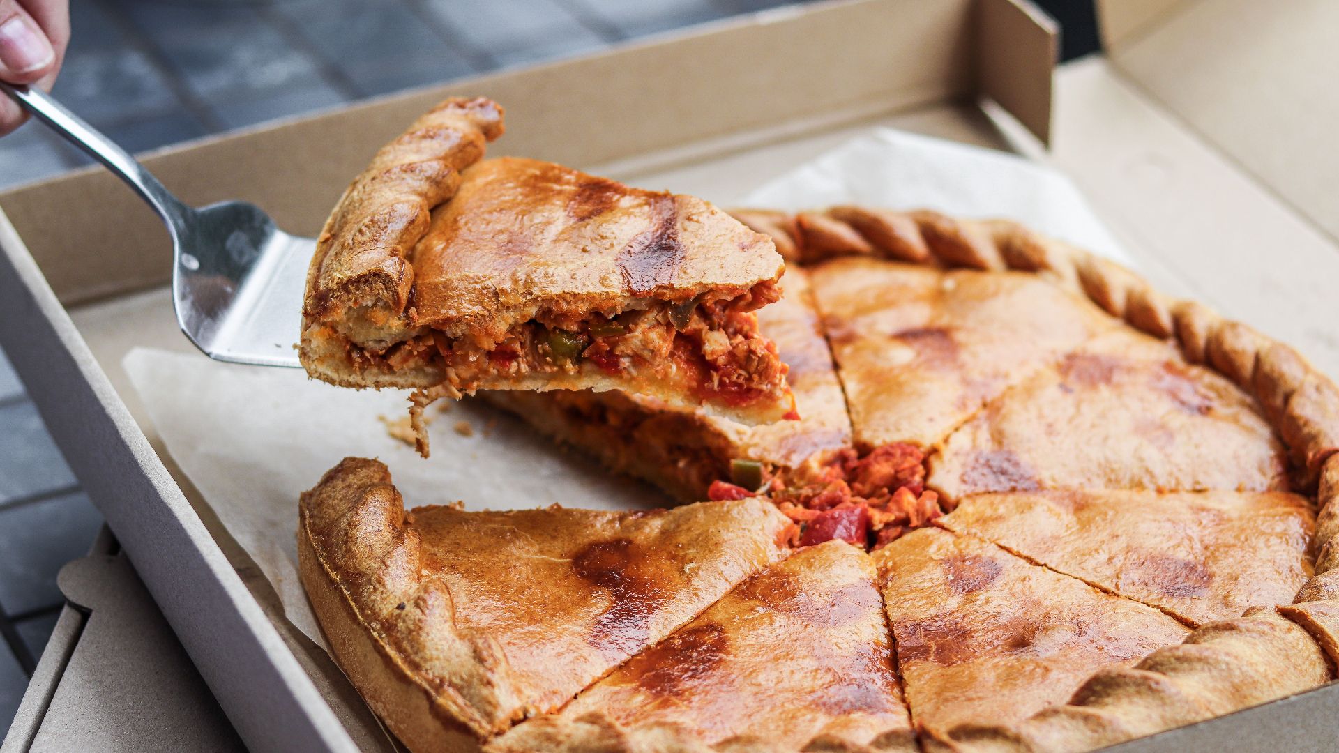 Close-up of a delicious deep-dish pizza slice being served from a cardboard box.