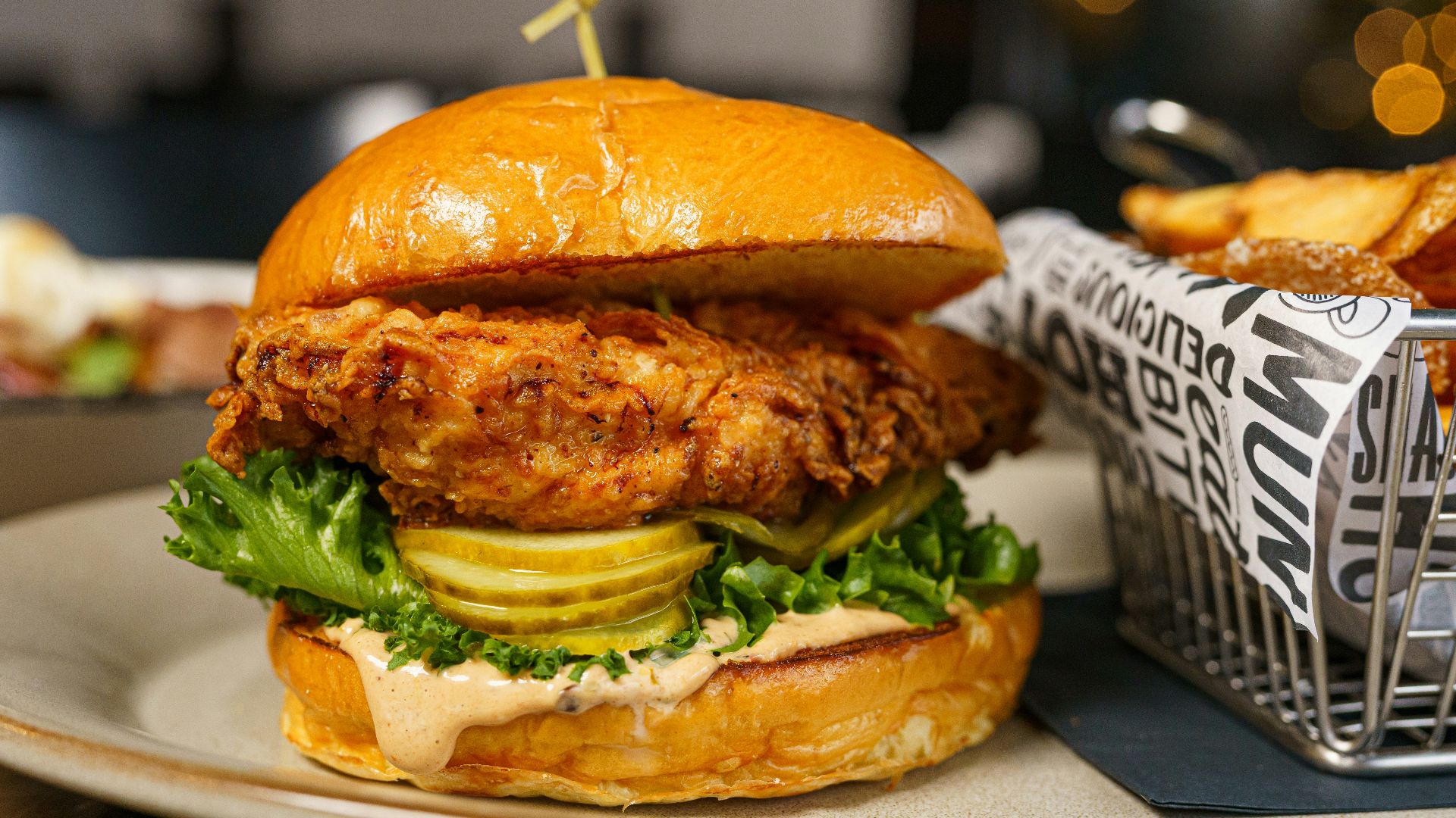 a chicken sandwich on a plate next to a basket of fries