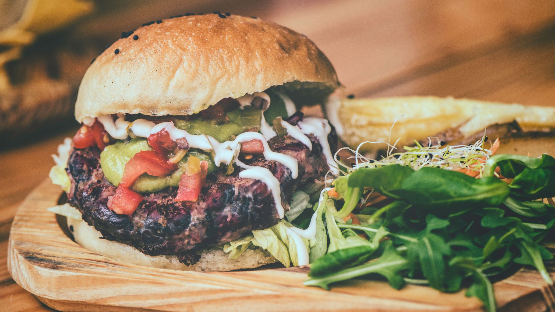 Delicious cheeseburger with fresh toppings and side of fries on a wooden board.