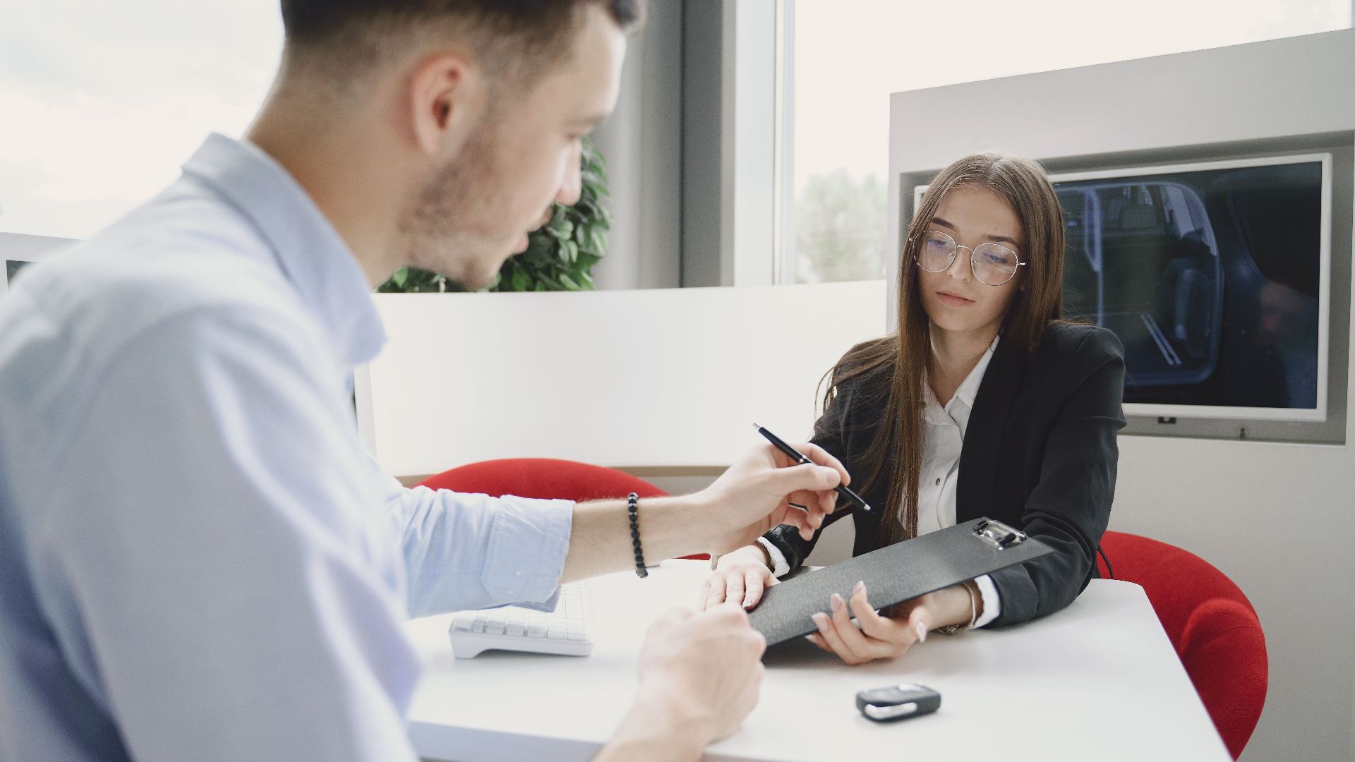 A man and woman discussing and signing a document at a table in an office setting.
