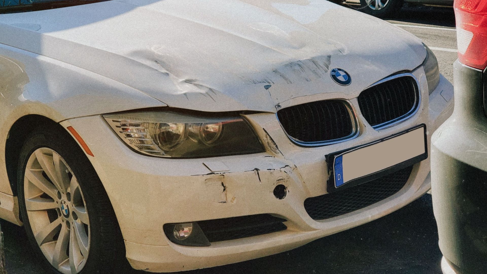 White BMW sedan with front-end damage parked on a busy city street.