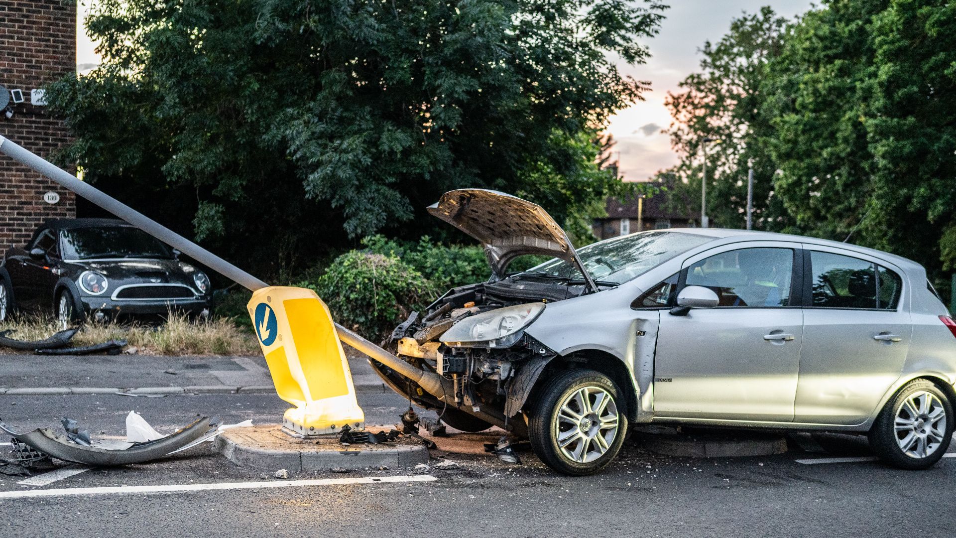 A damaged car that crashed into a lamp post on a London street during twilight.