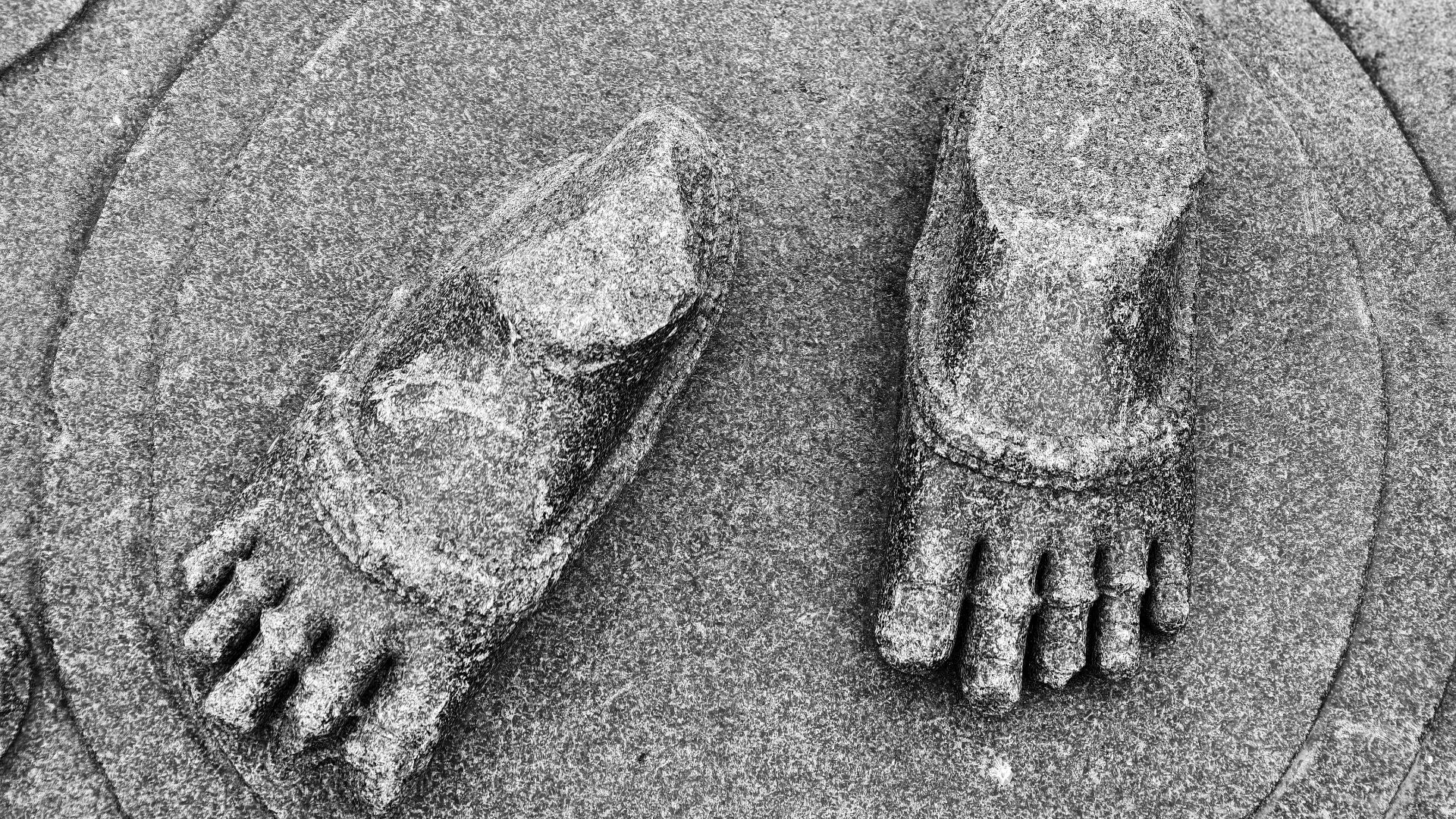 Black and white photo of ancient stone footprints engraved on granite, symbolizing history and tradition.