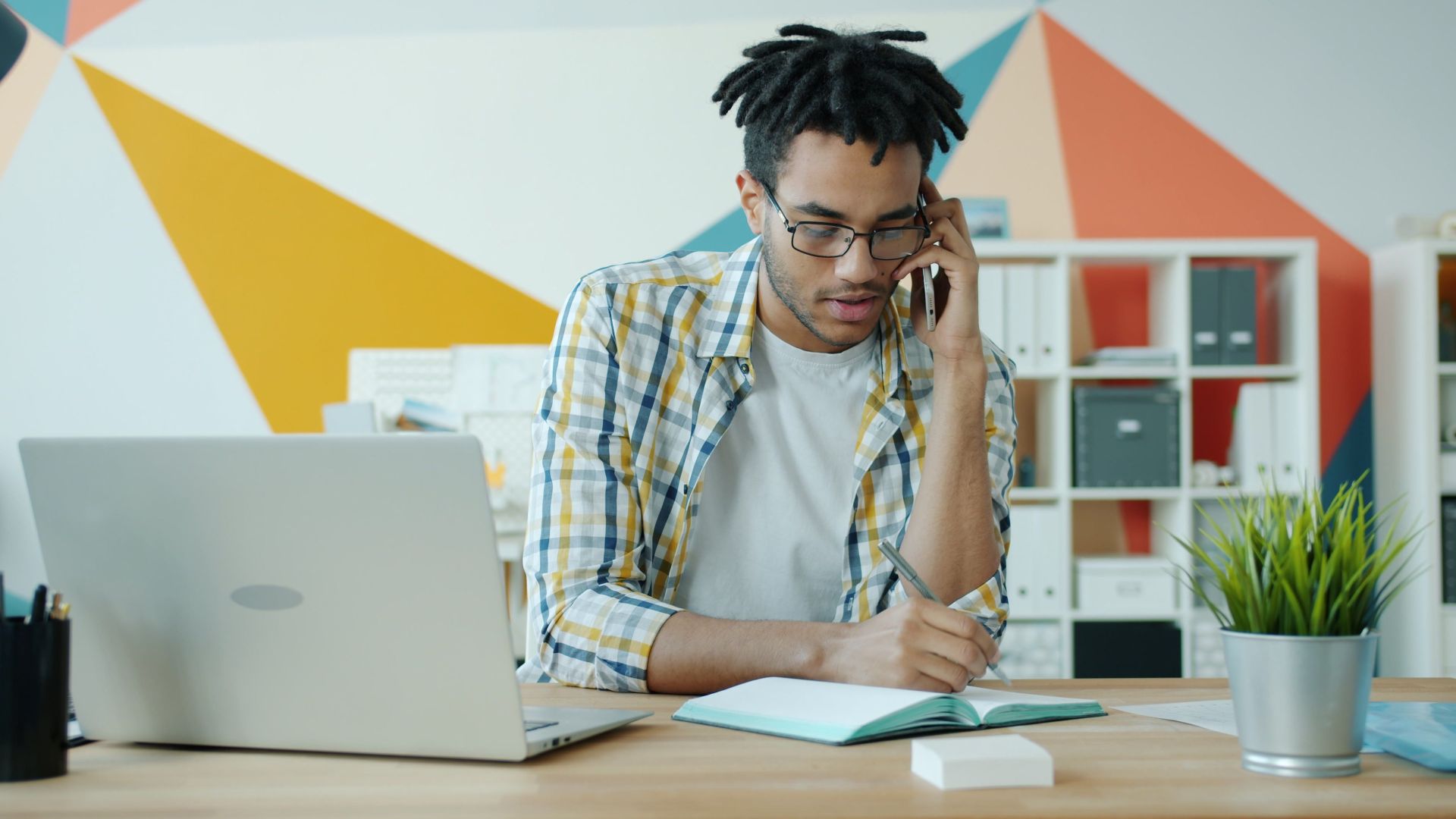 Young adult man in modern office multitasking on phone and laptop.