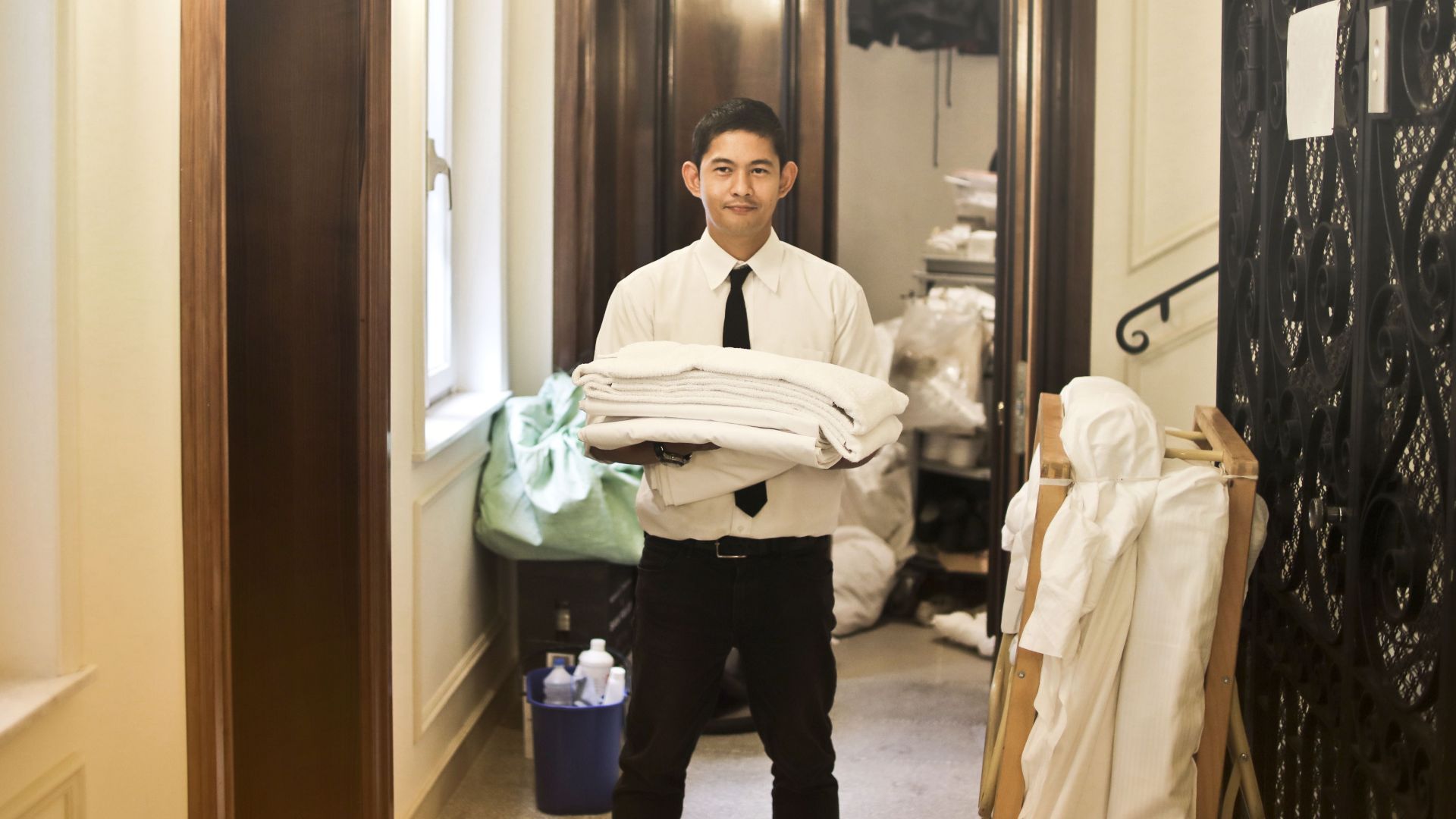 Professional hotel staff member carrying fresh linens in an elegant hallway.