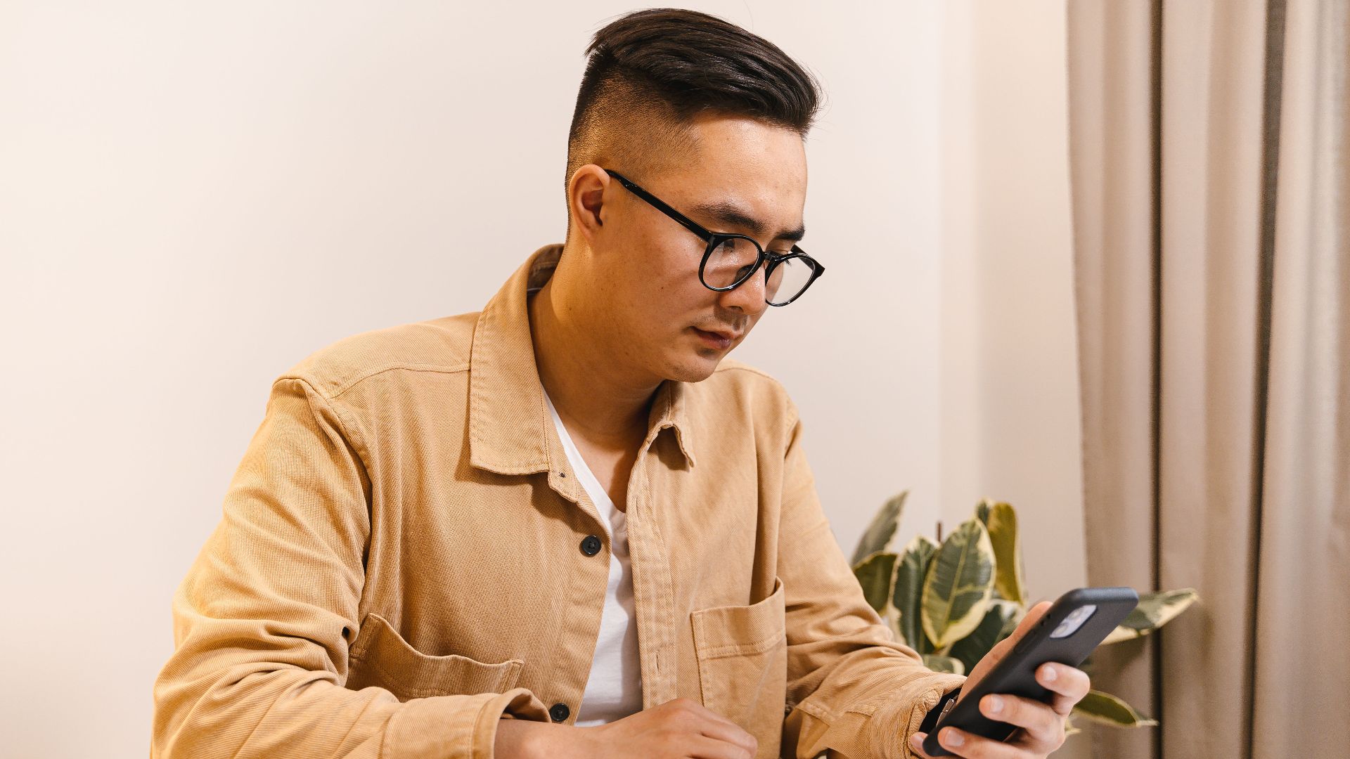 Adult male office worker concentrating on his smartphone and notebook at a desk indoors.