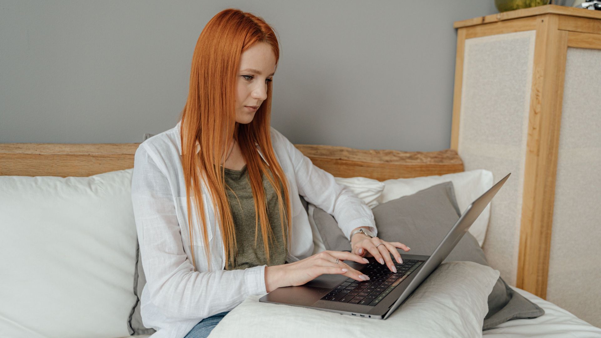 Red-haired woman focused on laptop work from home setting.