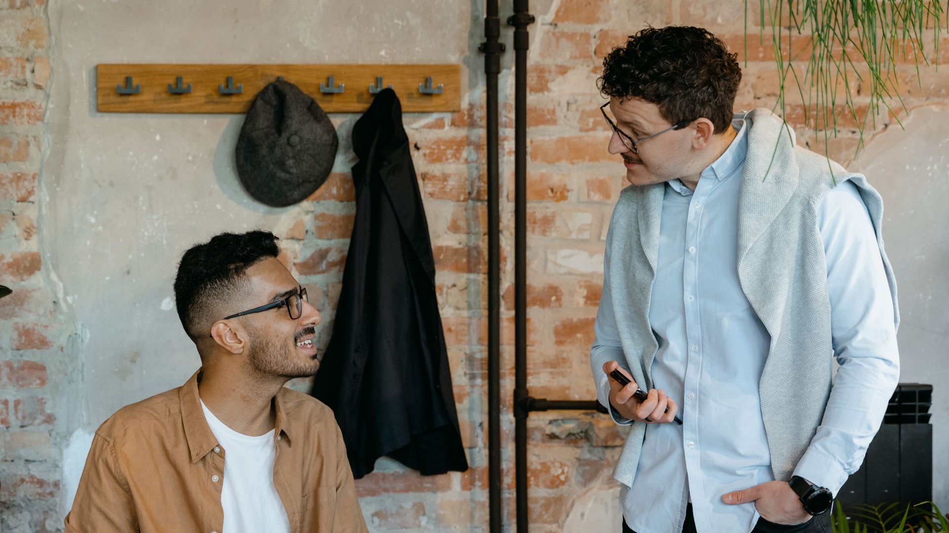 Two men discussing ideas in a stylish office with exposed brick walls.
