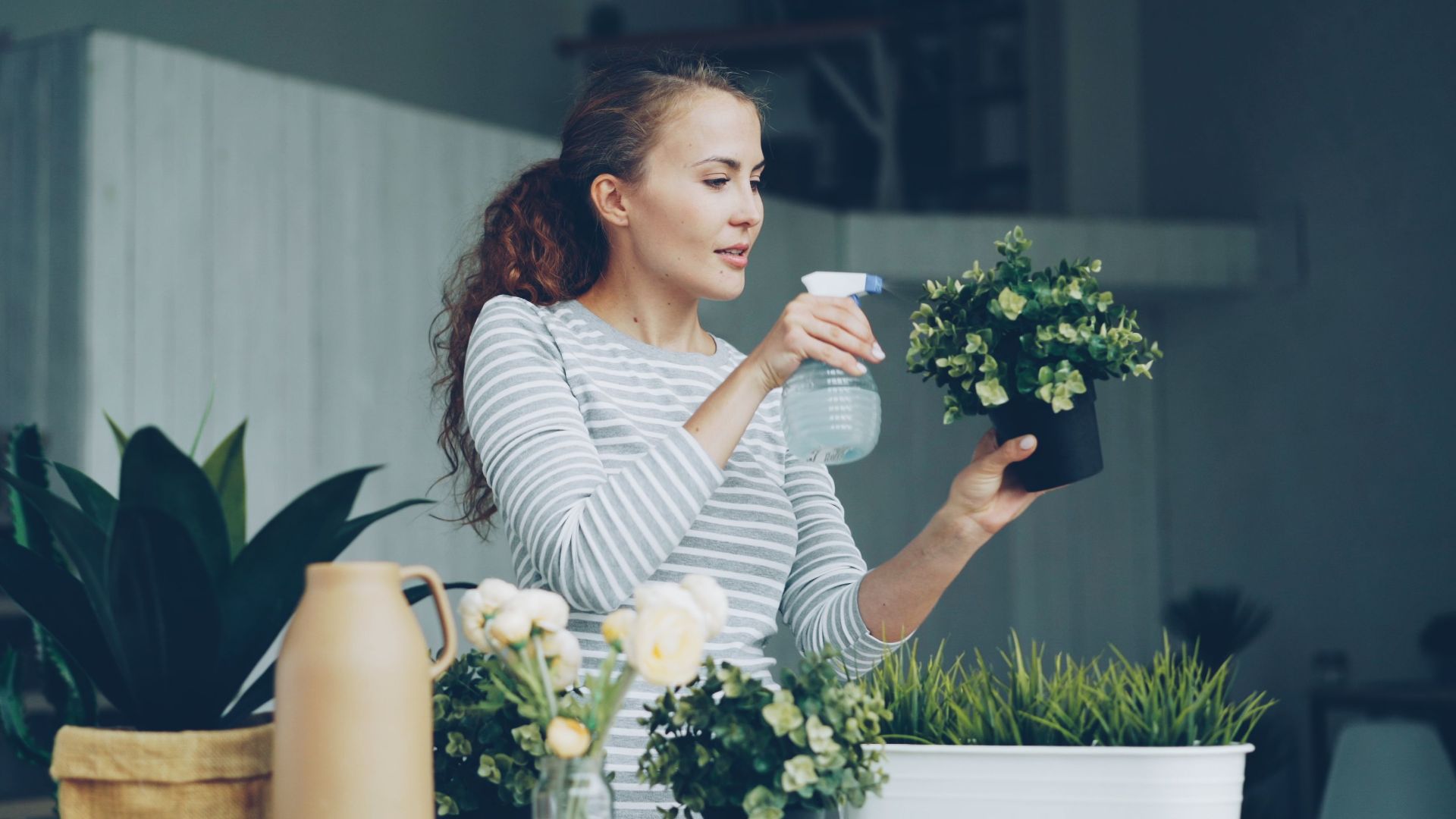 A woman waters potted plants indoors, enjoying a gardening moment at home.