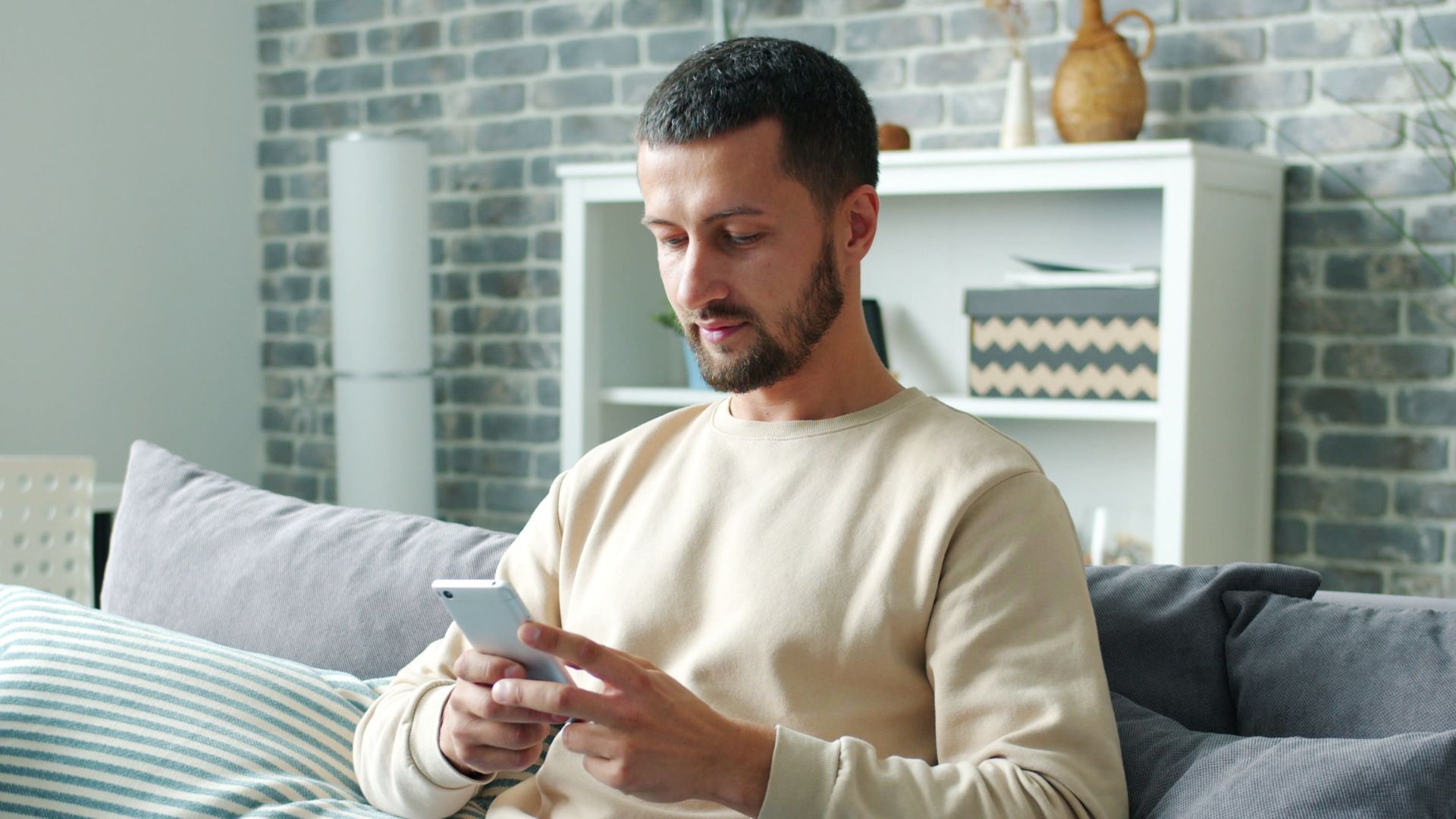 Man sitting on a couch using a smartphone in a cozy living room setting.