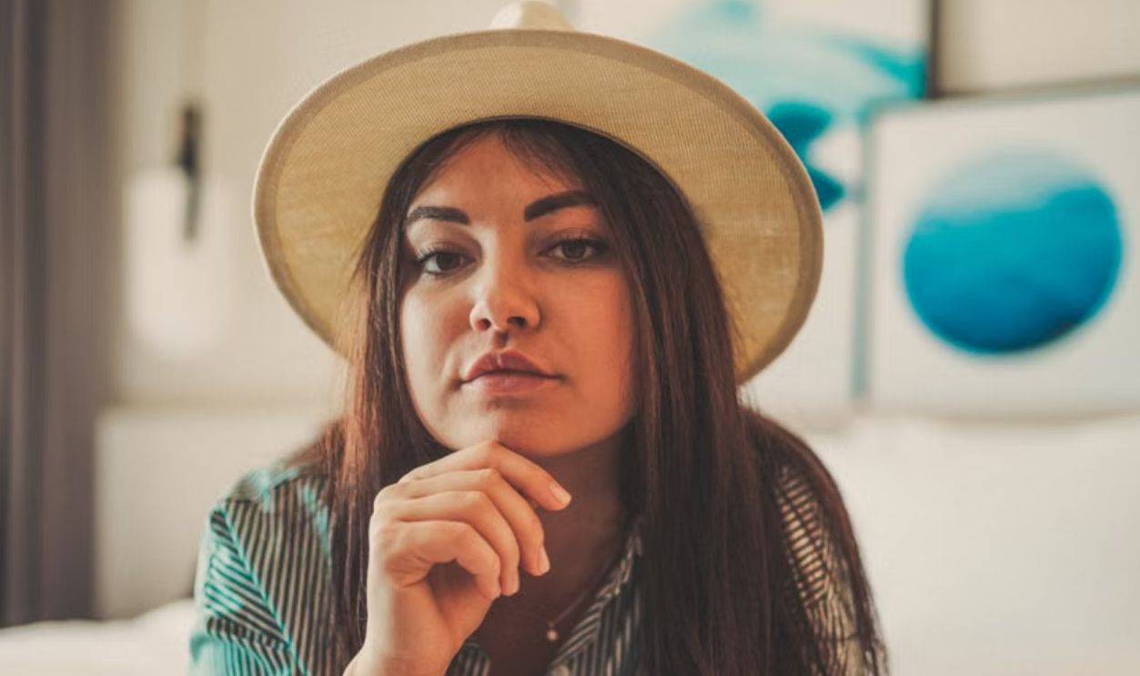 Woman with sun hat resting on bed in stylish indoor setting with modern art decor.