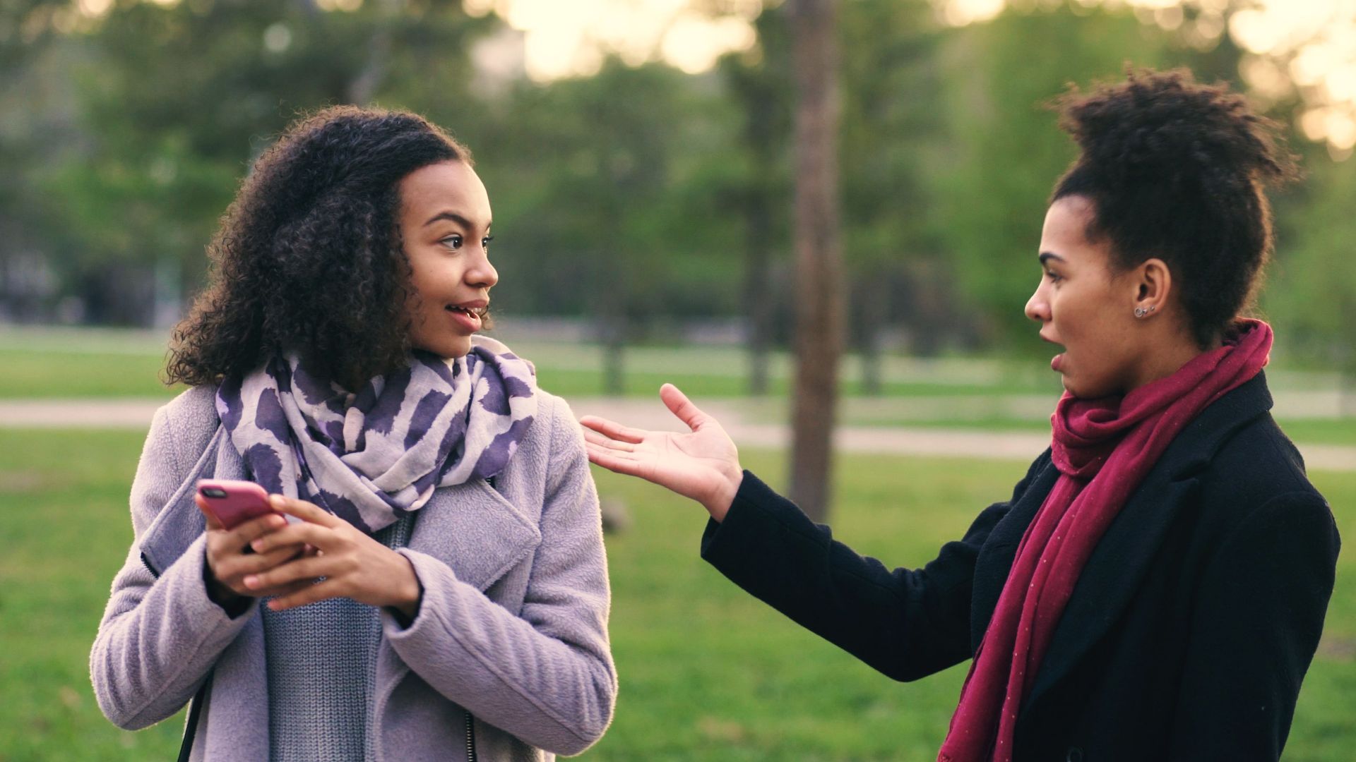 Two women having a conversation outdoors with trees in the background.