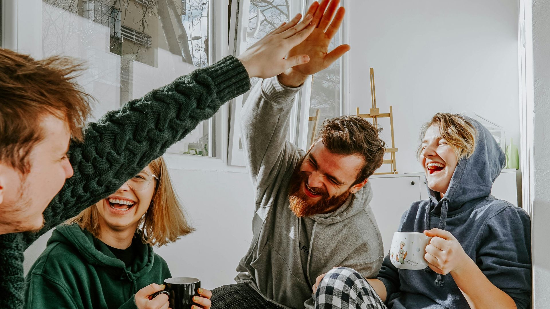 four friends laughing and high fiving over coffee