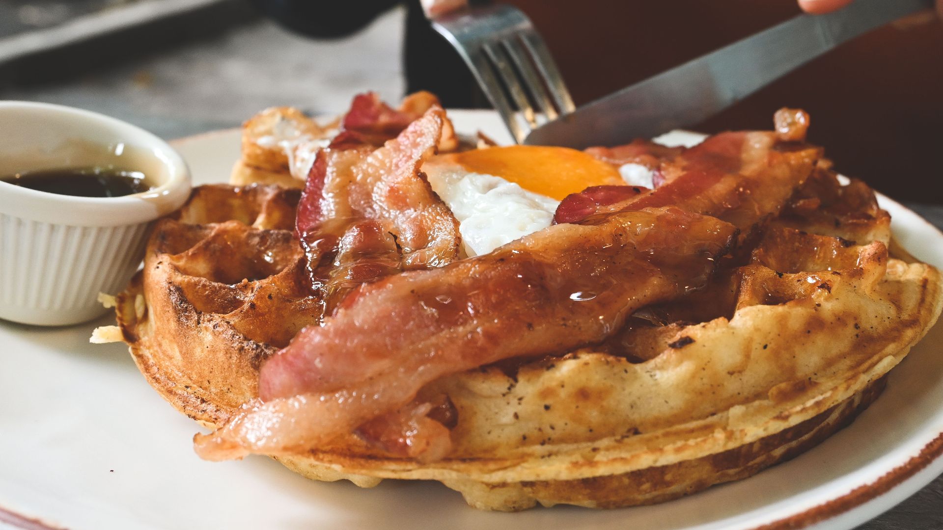Delicious breakfast waffle topped with crispy bacon, sunny-side-up egg, and maple syrup.