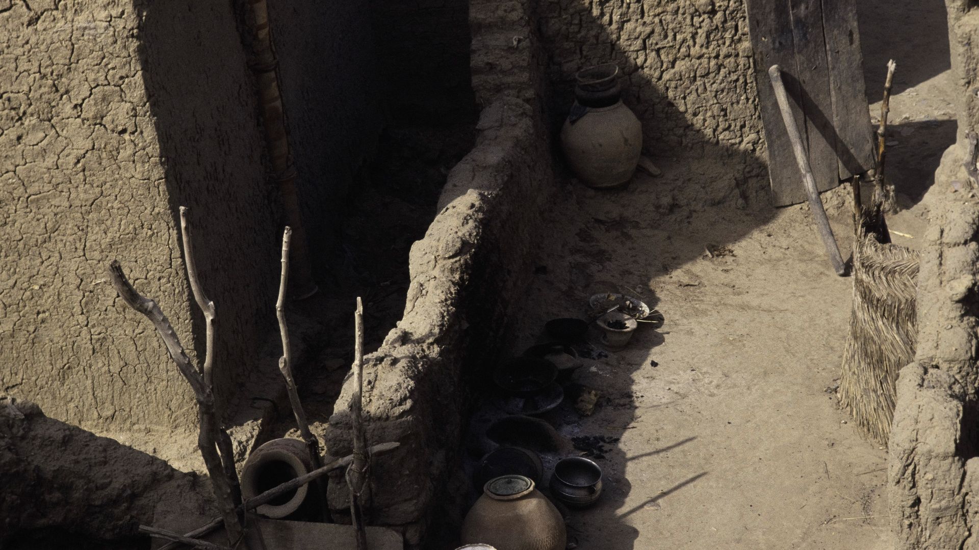A courtyard with pots between mud walls seen from a roof terrace.