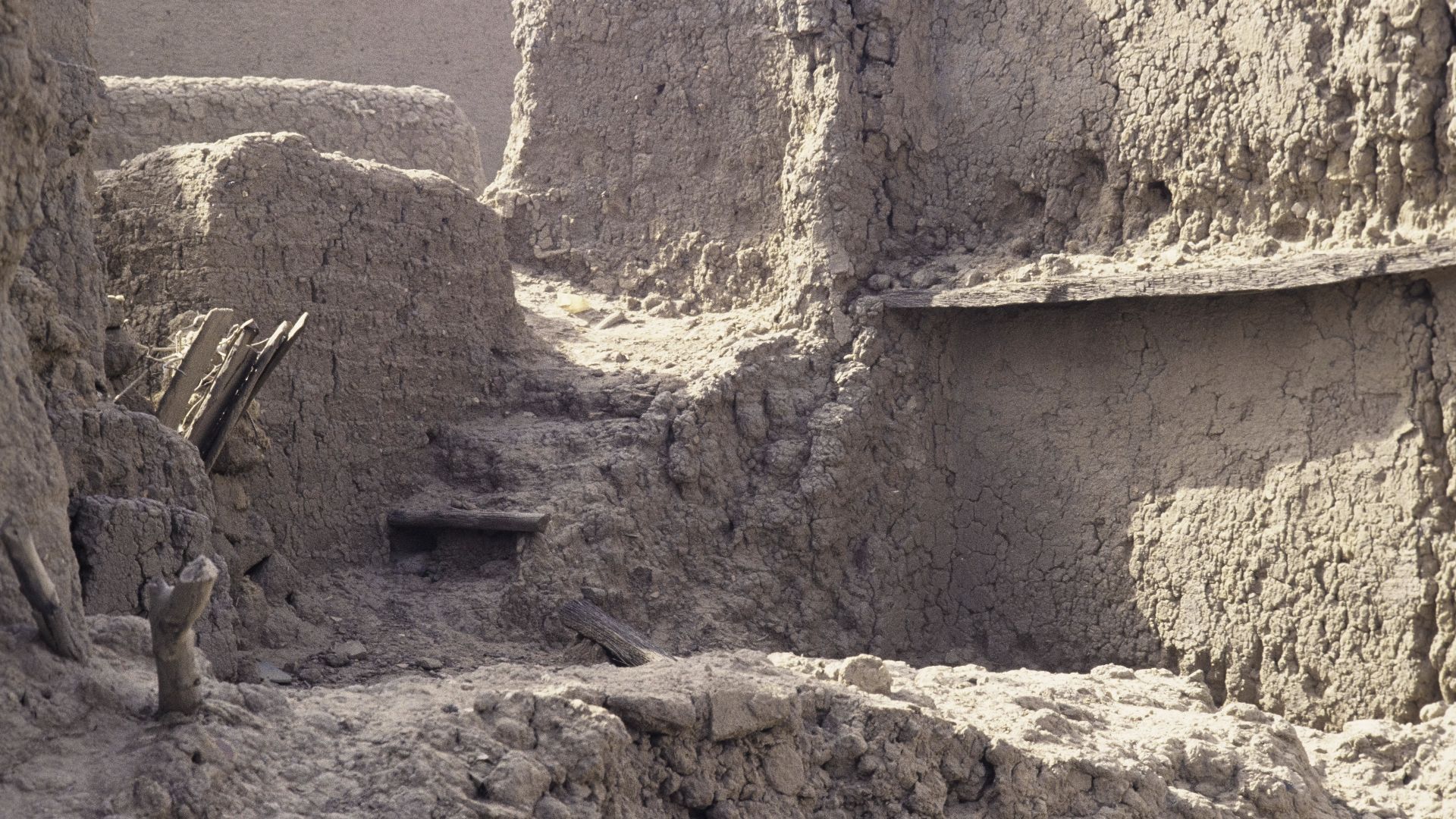 A dilapidated clay construction of walls with protruding wooden sticks and planks.