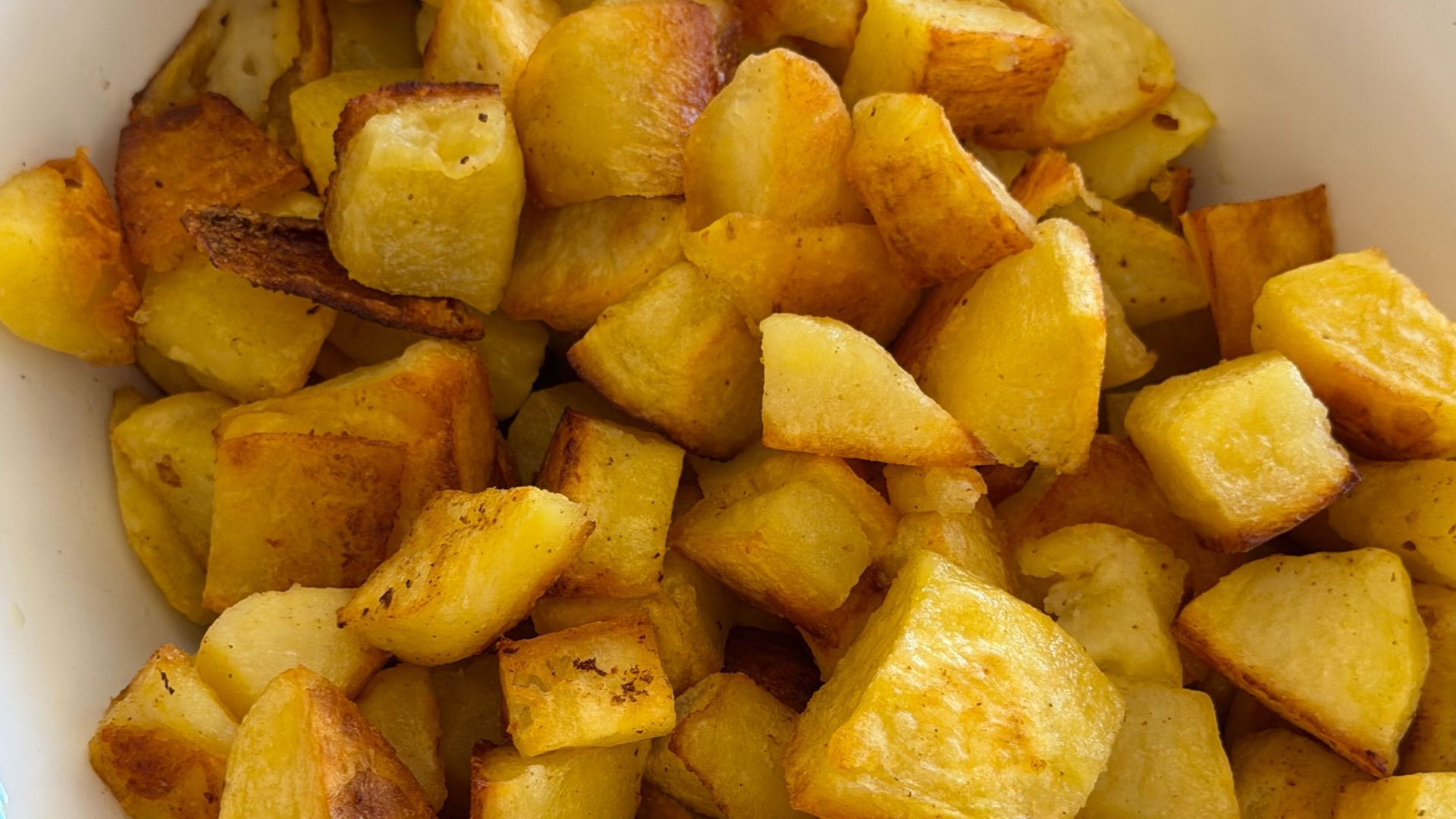A close-up of perfectly roasted golden potato cubes served in a white bowl, showcasing appetizing textures.